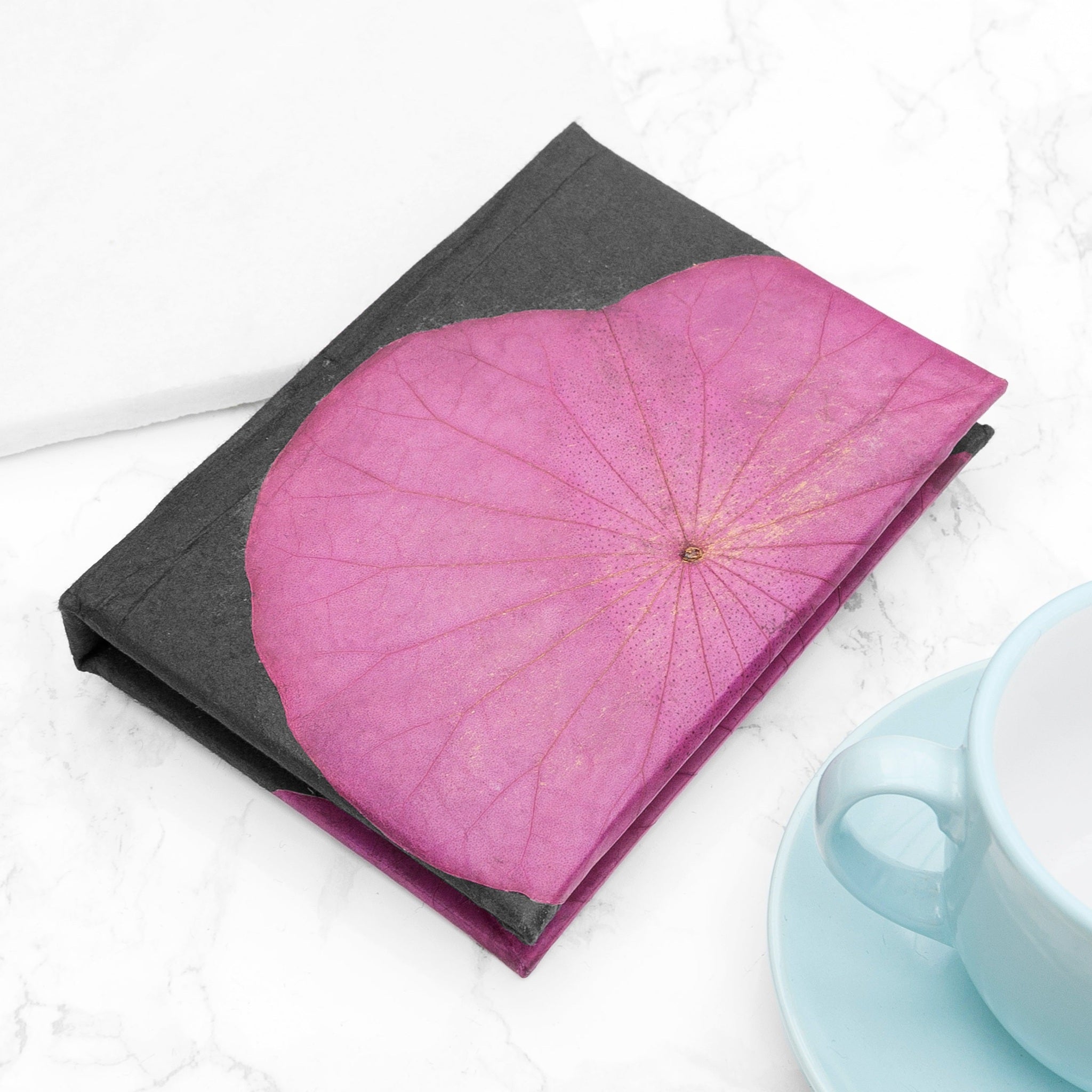Pink leaf-shaped flower design on a black book with a blue cup and saucer in the background