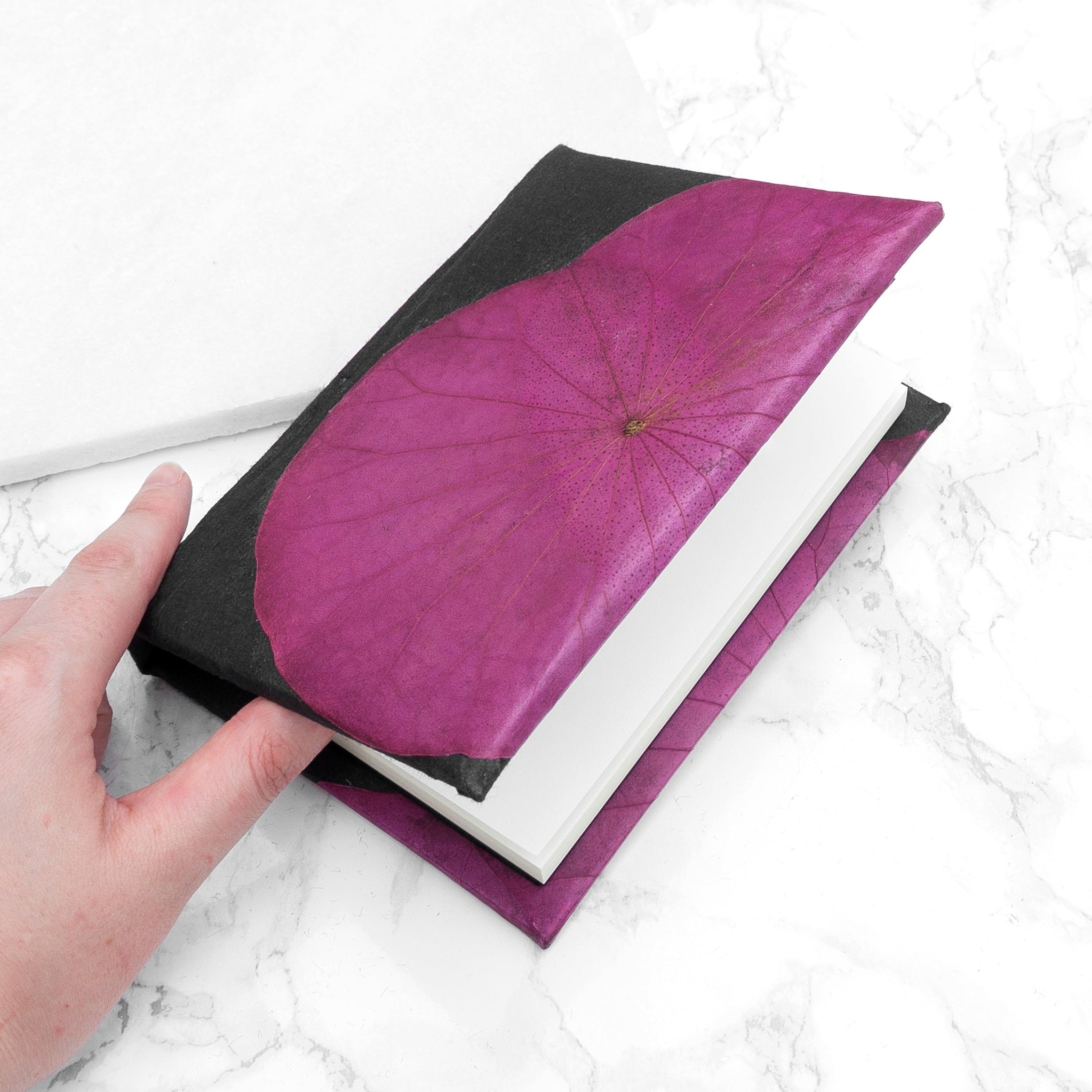 Hand holding a black and purple notebook on a marble surface