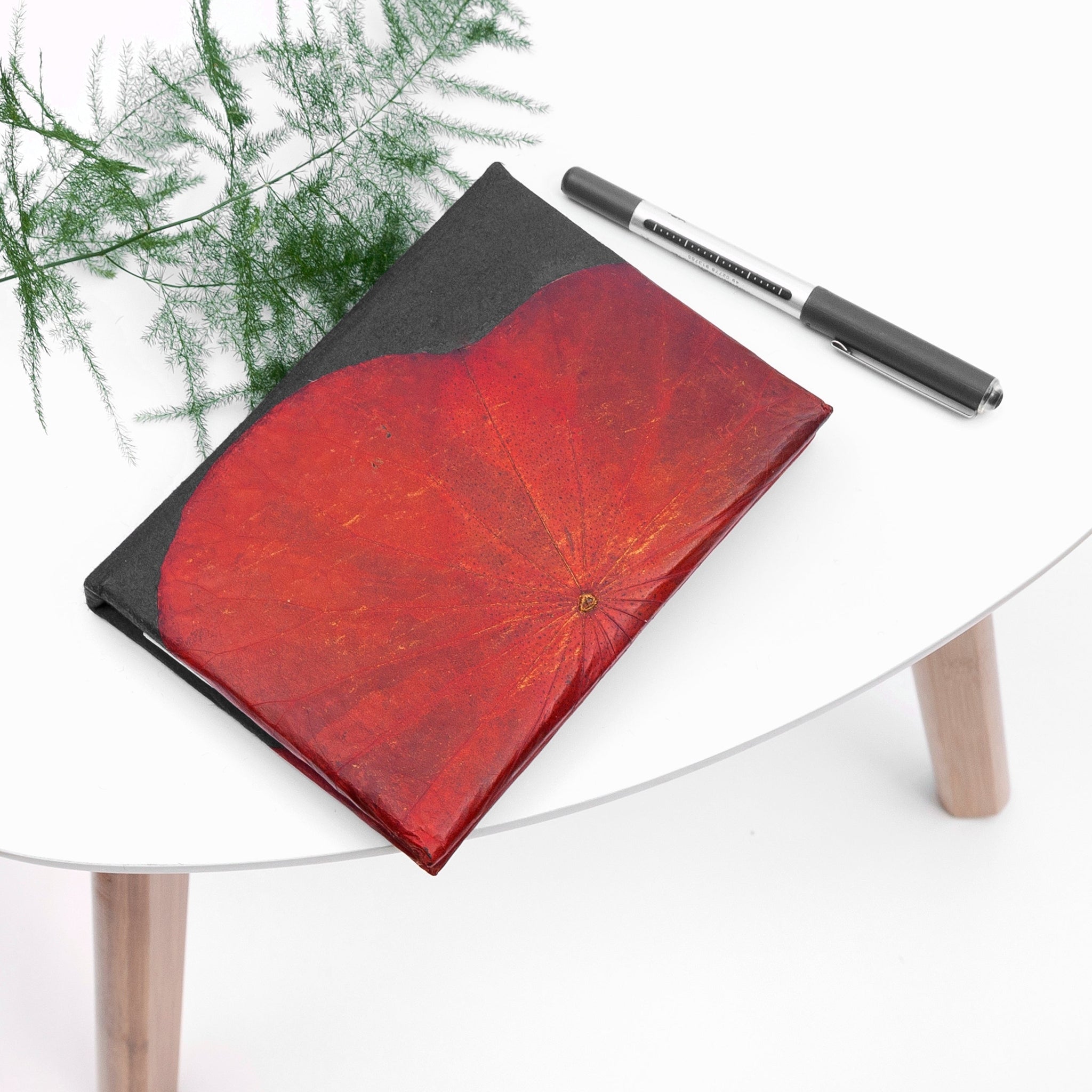 Notebook with red leaf design and pen on a glass table