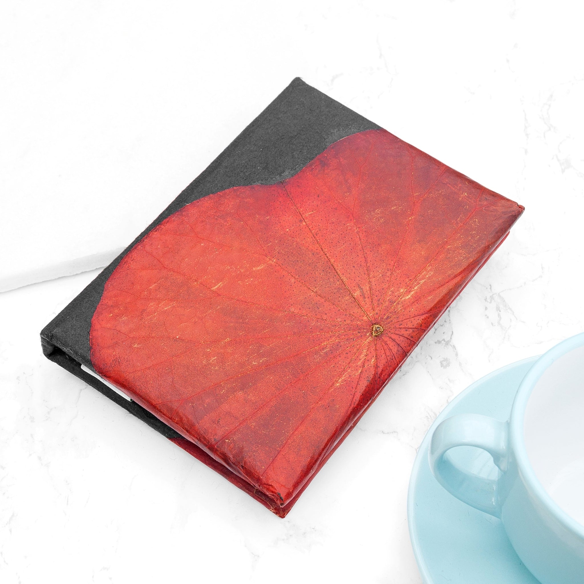 Red notebook on a white surface next to a light blue cup.