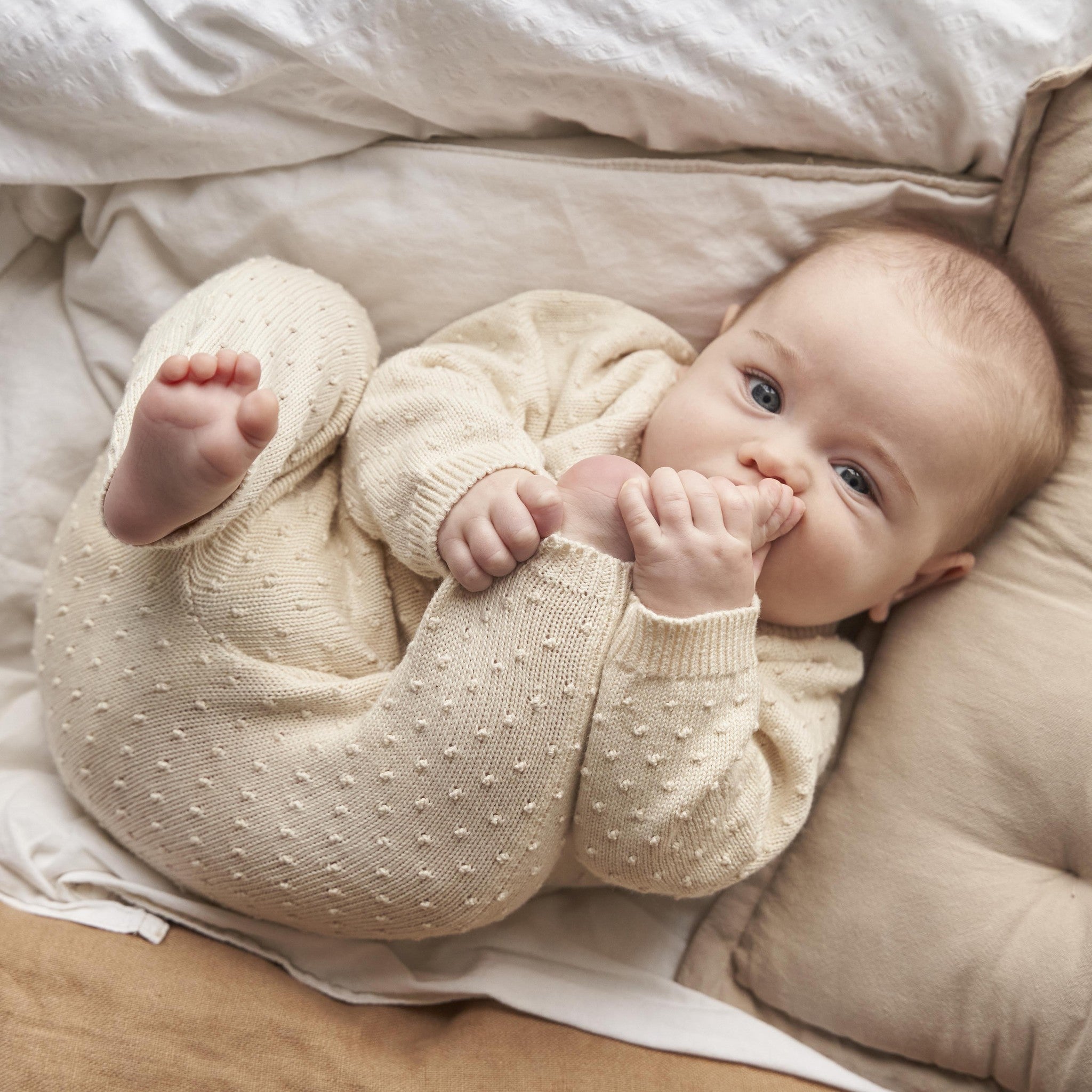 Baby in a cream-colored outfit lying on a bed