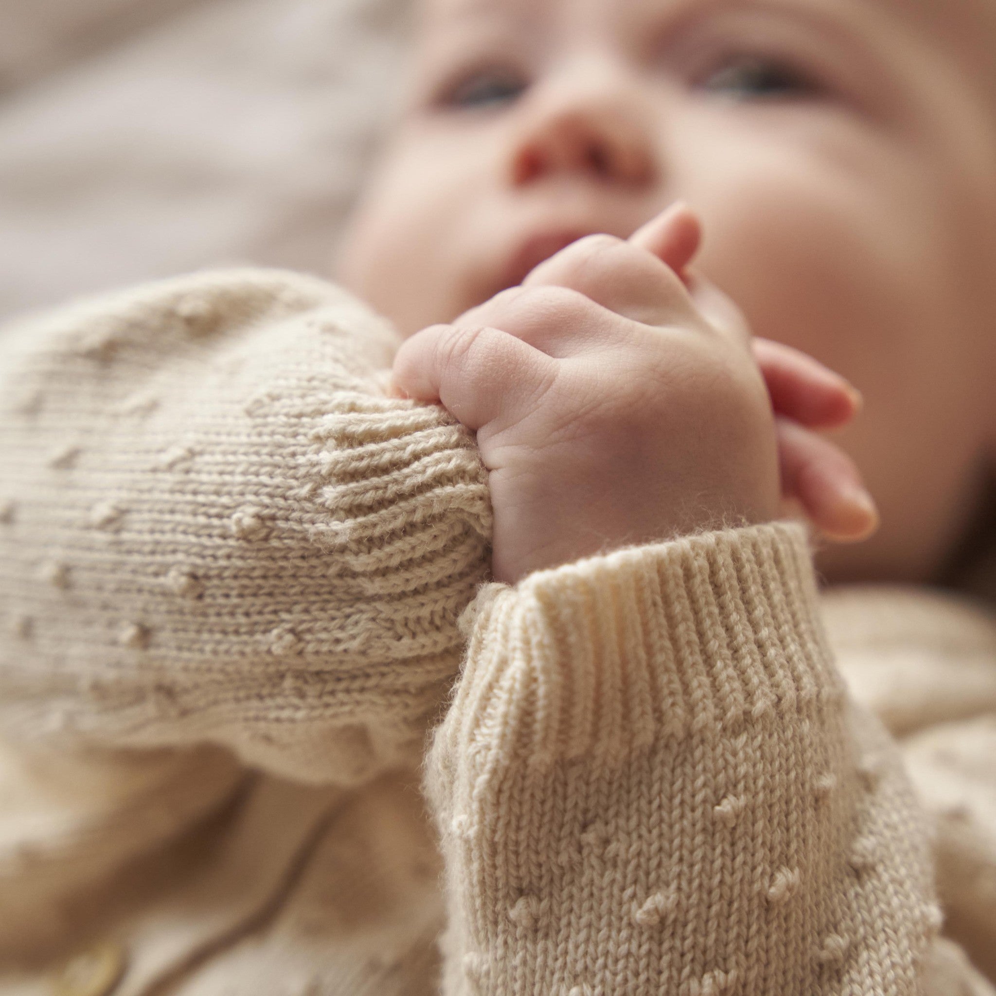 Close-up of a baby wearing a beige knitted sweater with a blurred background