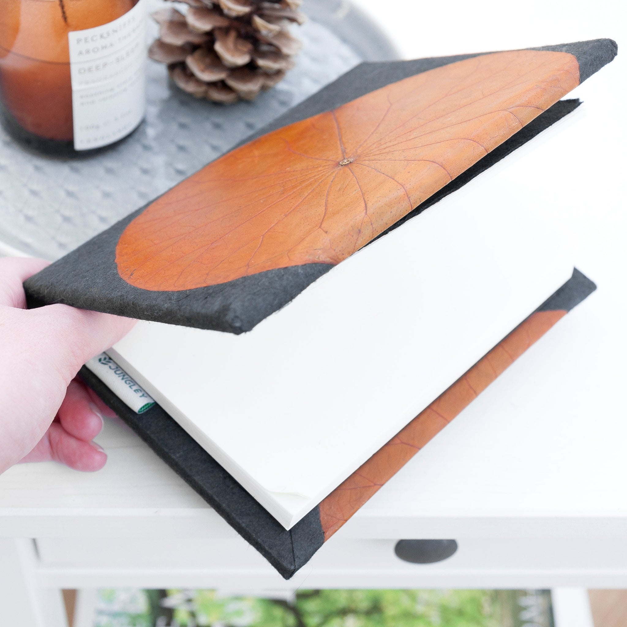 Notebook with a decorative cover featuring a leaf design held by a hand.