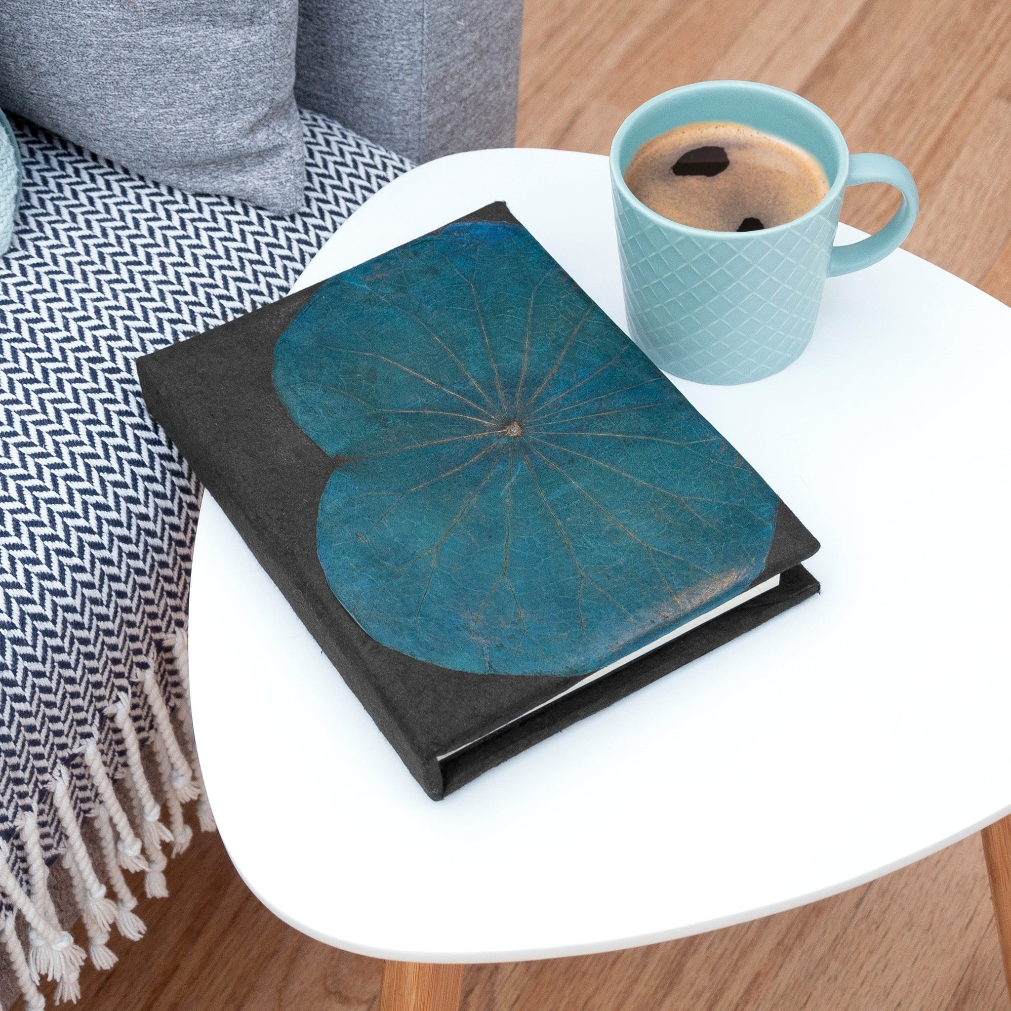 Teal notebook and blue mug on a white table with a gray cushioned chair.