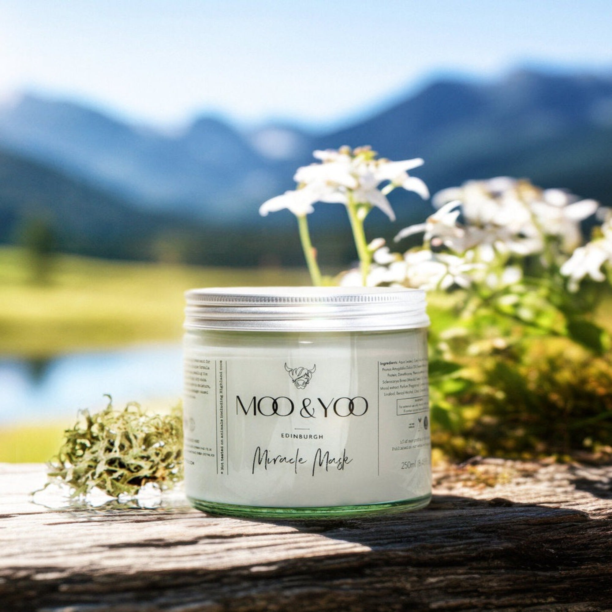 Jar of 'Moo & Yoo' product on a wooden surface with a scenic background