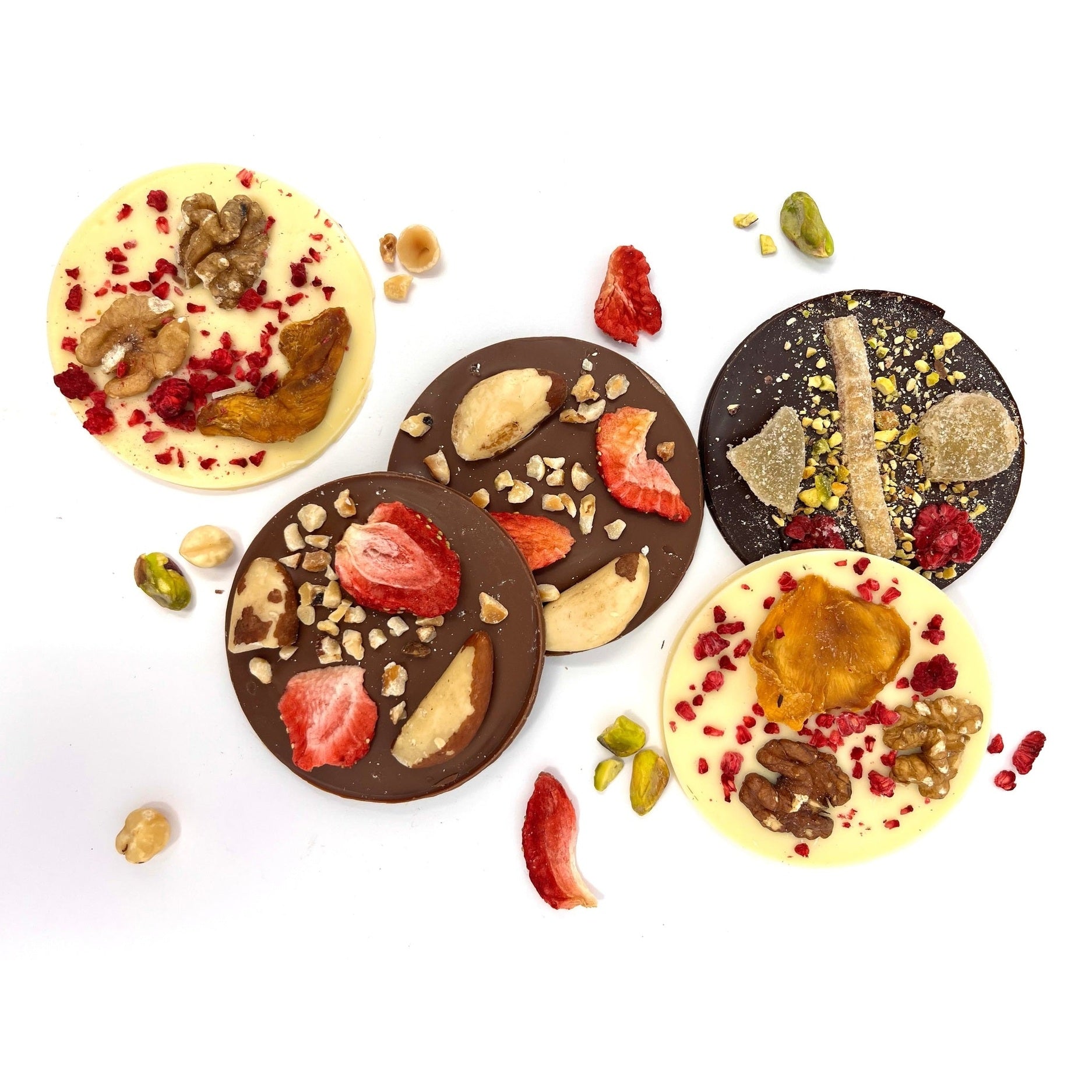 Assorted chocolate discs with fruits and nuts on a white background