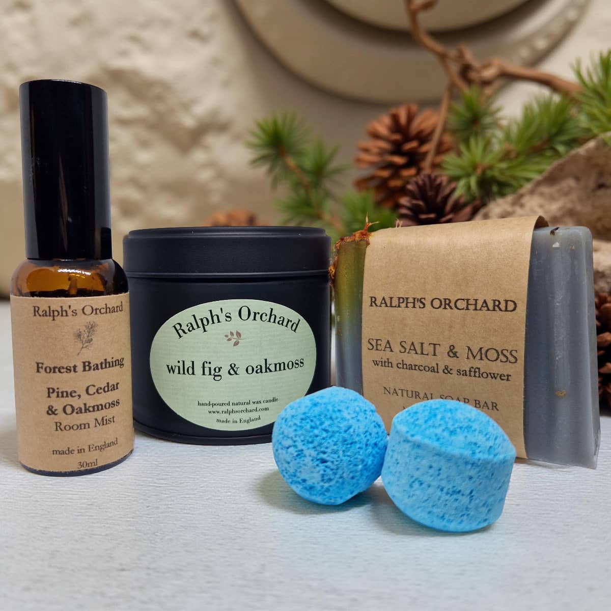 Collection of Ralph's Orchard products including a bottle, jar, and bath bombs on a textured surface with a natural background.