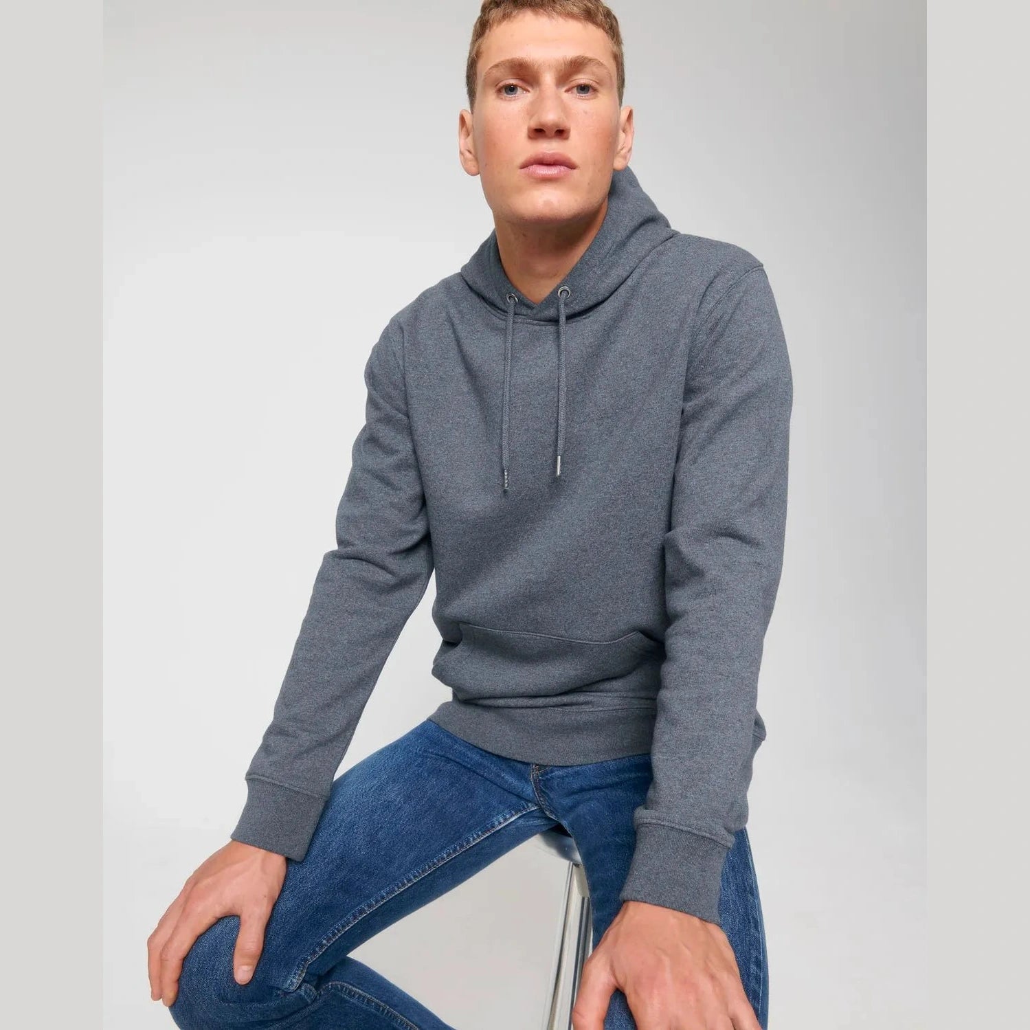Man wearing a gray hoodie and blue jeans on a light gray background