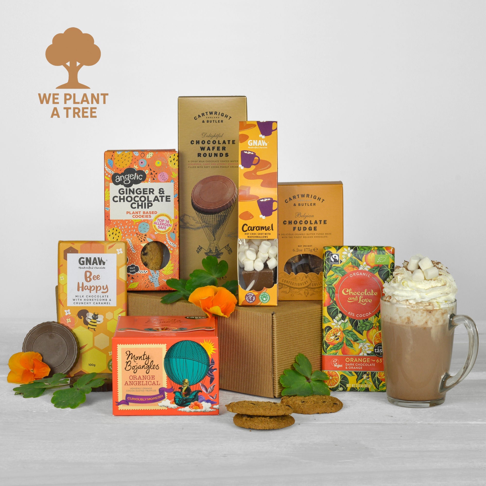 Assorted chocolate products with packaging and a hot chocolate mug on a light gray background, featuring the 'We Plant a Tree' brand logo.