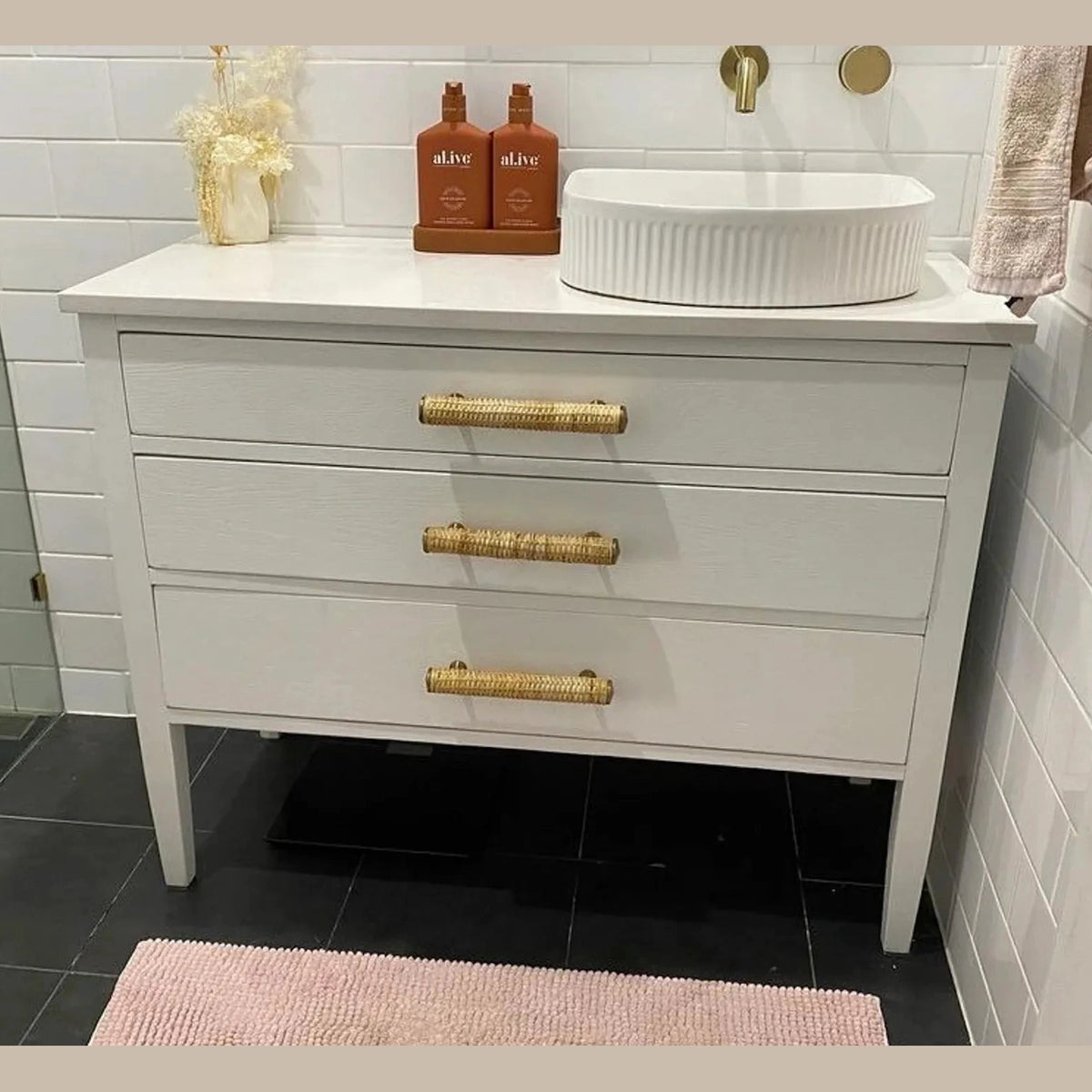 Dunstanburgh rattan bar handles on three drawers beneath a white bathroom basin