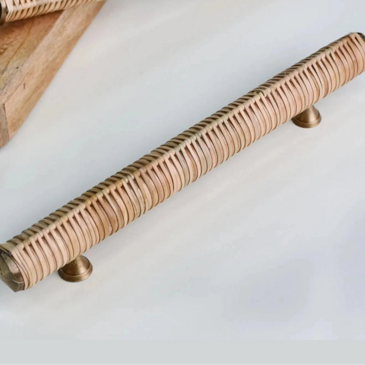 Long Druridge rattan-wrapped bar handle with metal mounting feet on a pale surface
