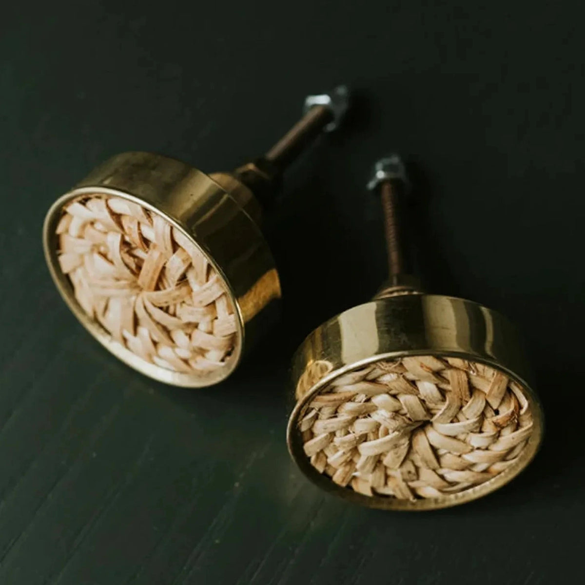 Two Dunstanburgh round knobs with woven rattan centres and antique brass-finish rims on a dark background