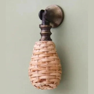 Dunstanburgh woven rattan drop handle with antique brass-finish mounting hardware on a pale green door