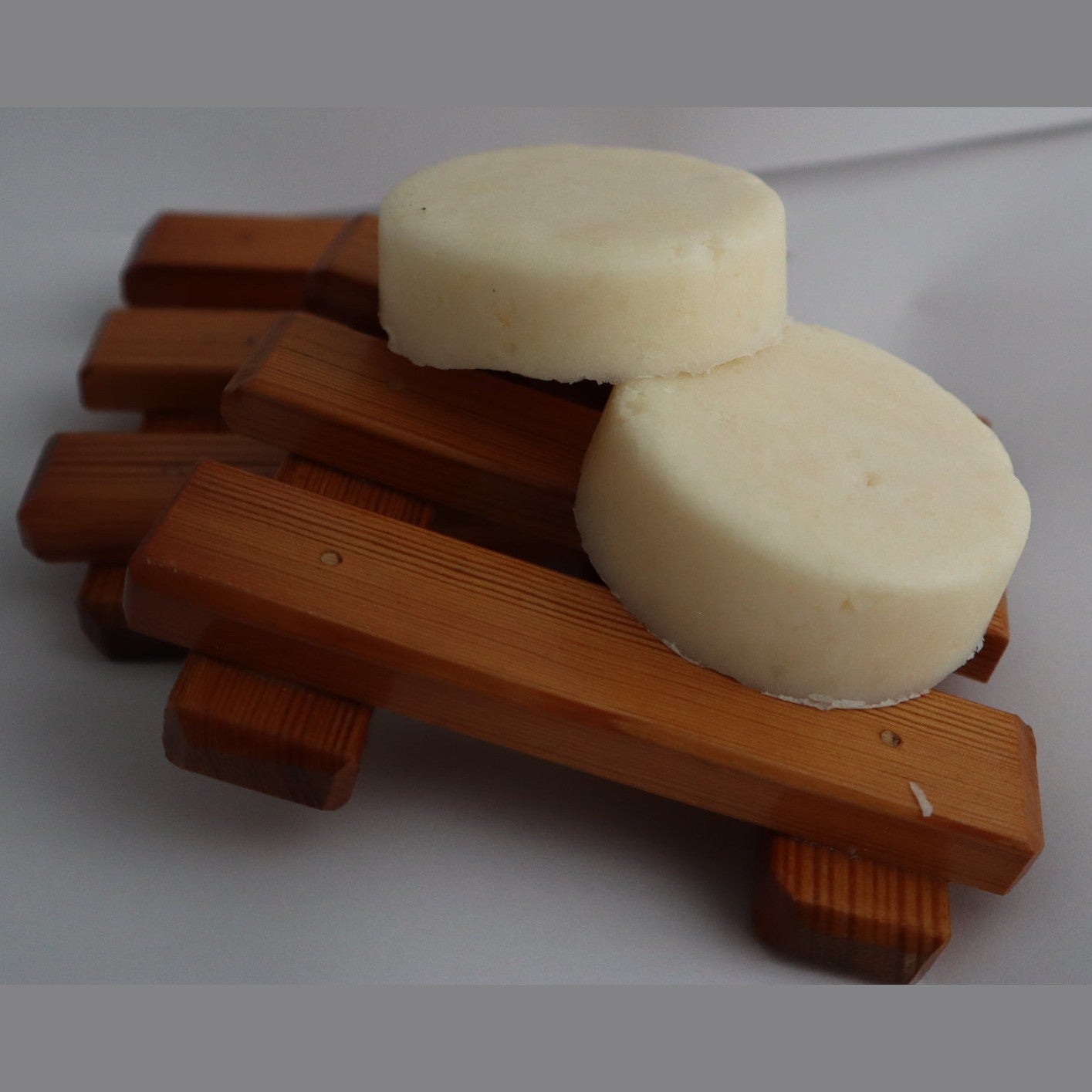 Two round white plastic-free shampoo bars on a wooden stand against a grey background