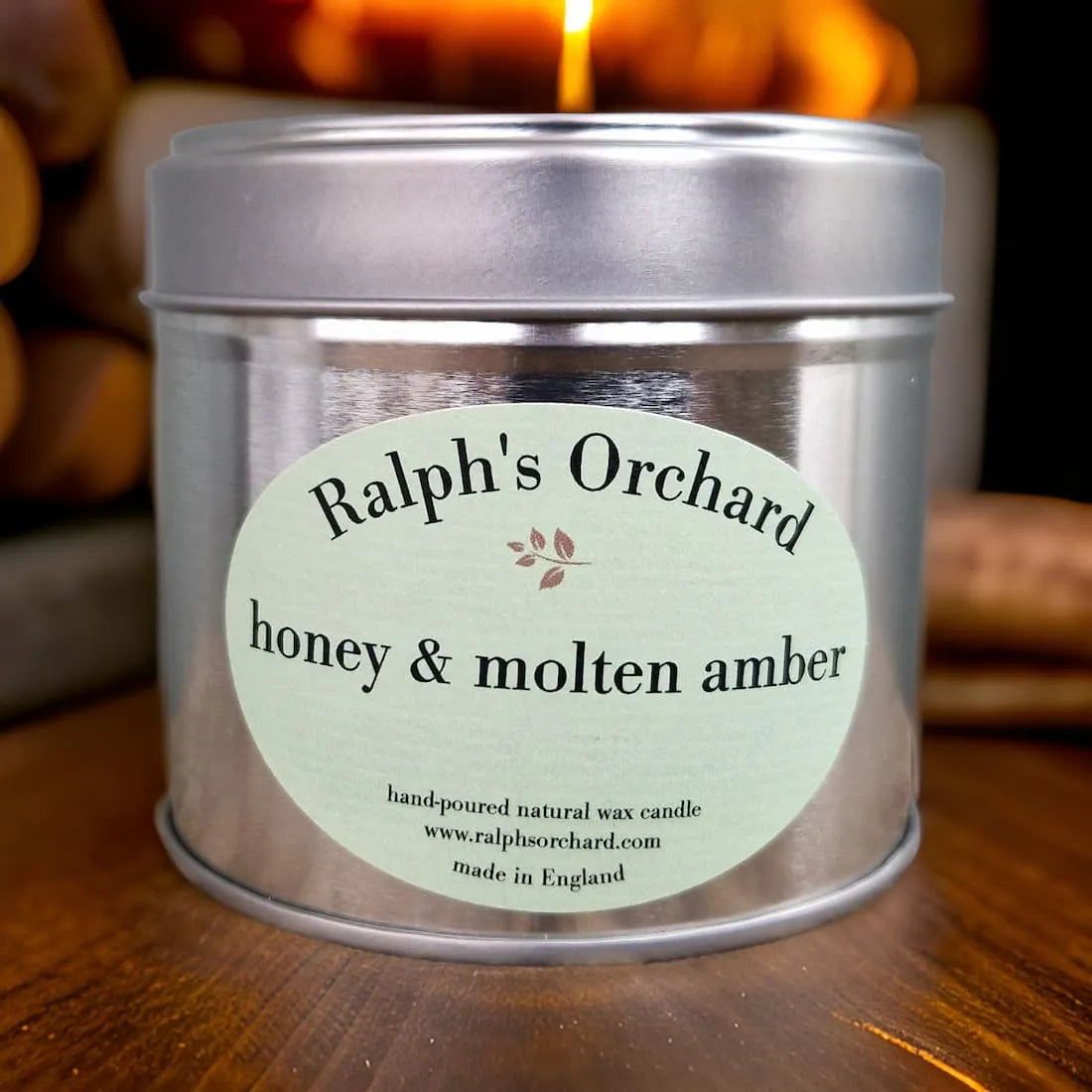 Candle tin labeled 'Ralph's Orchard honey & molten amber' on a wooden surface with a blurred background.
