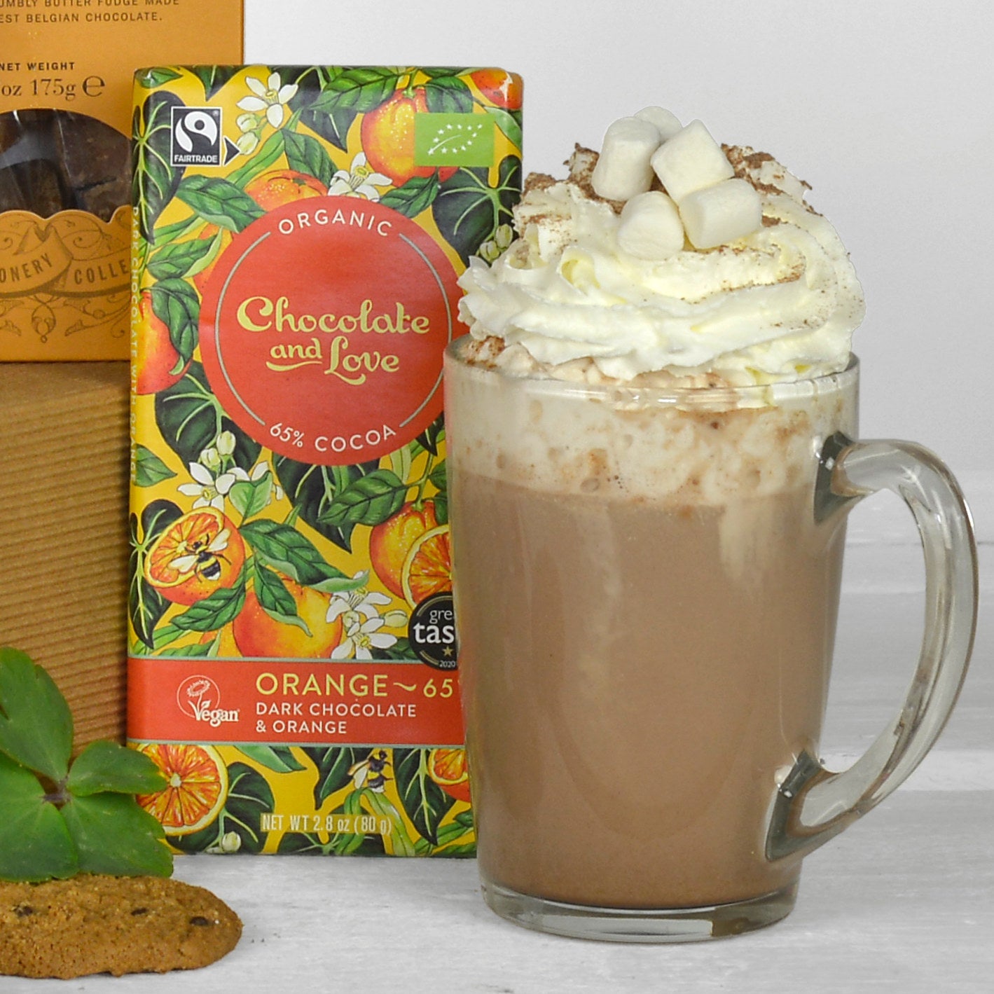 Hot chocolate with whipped cream and marshmallows next to a box of Organic Chocolate and Love dark chocolate.