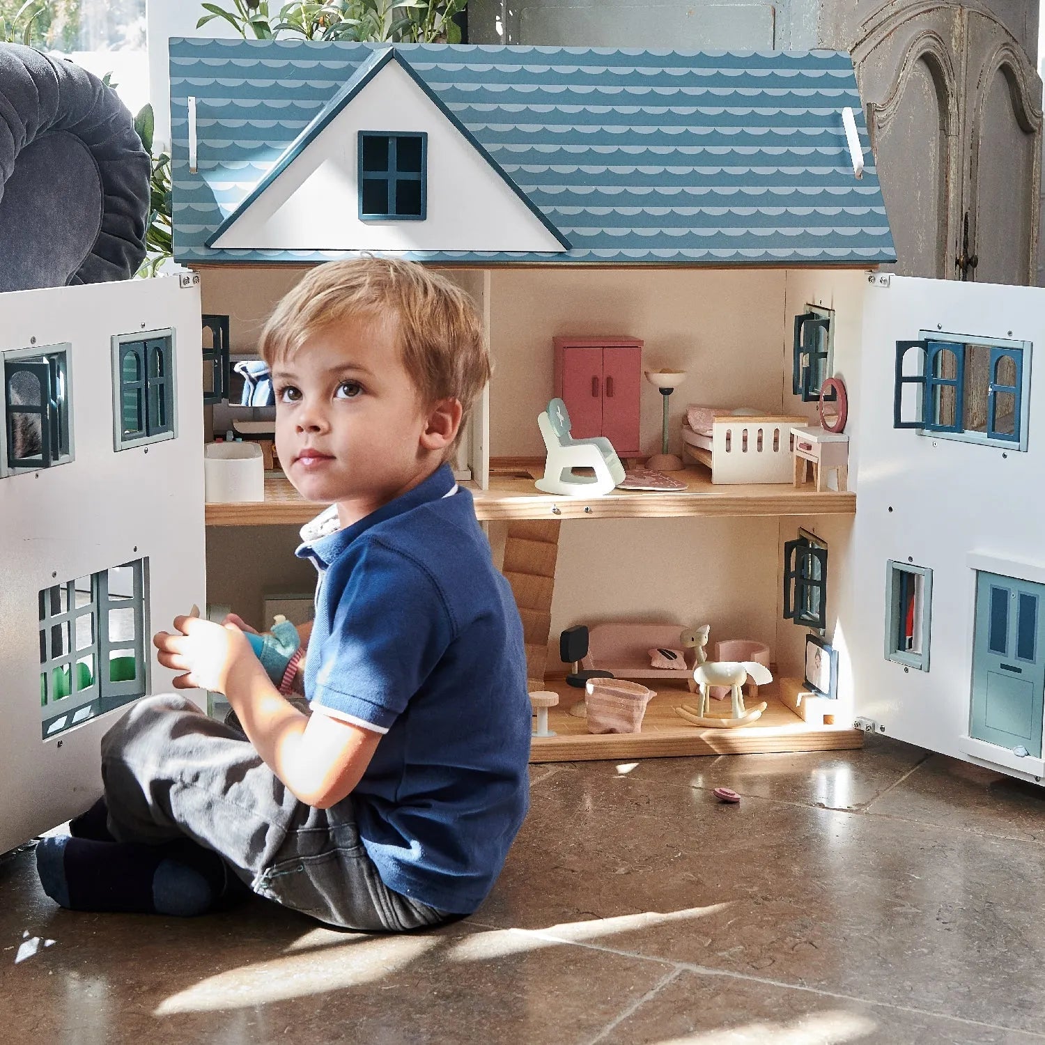 Child playing with a dollhouse toy set in a room.