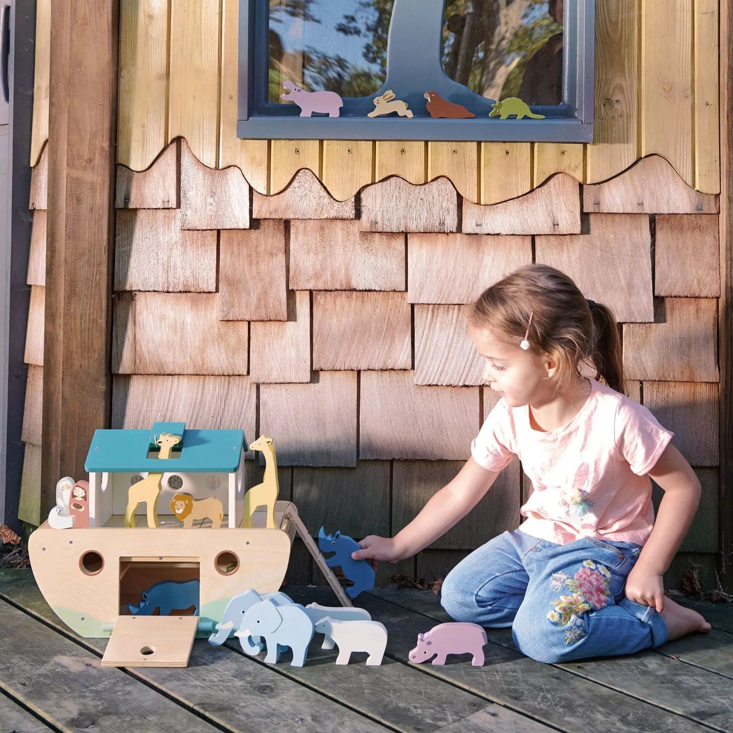 Child playing with wooden toys in front of a wooden playhouse