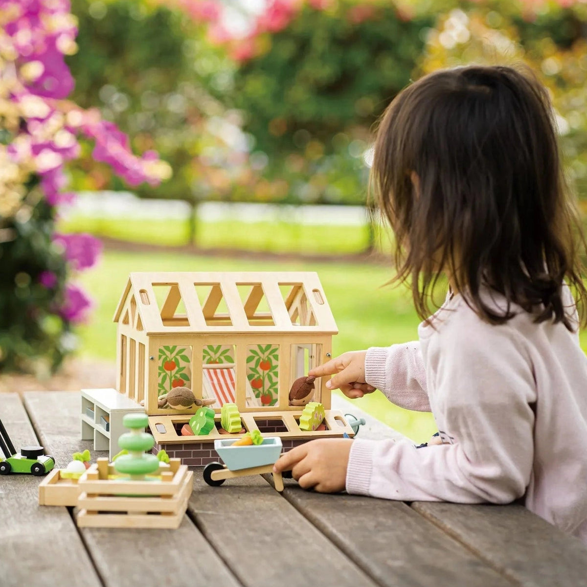 Child playing with the Tender Leaf greenhouse and miniature garden accessories on an outdoor wooden table