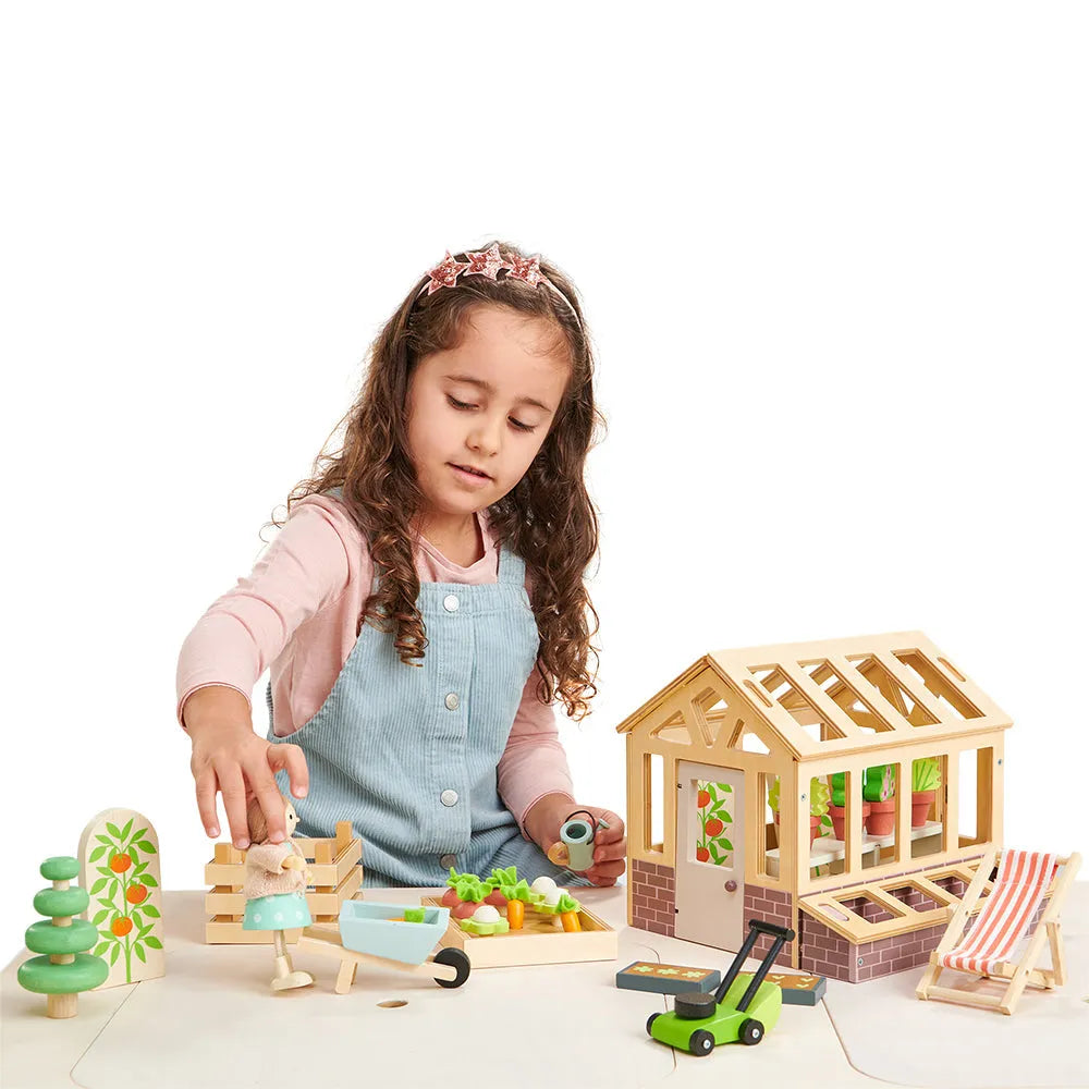 Child playing with the Tender Leaf greenhouse and garden set, with a doll beside the miniature vegetable bed