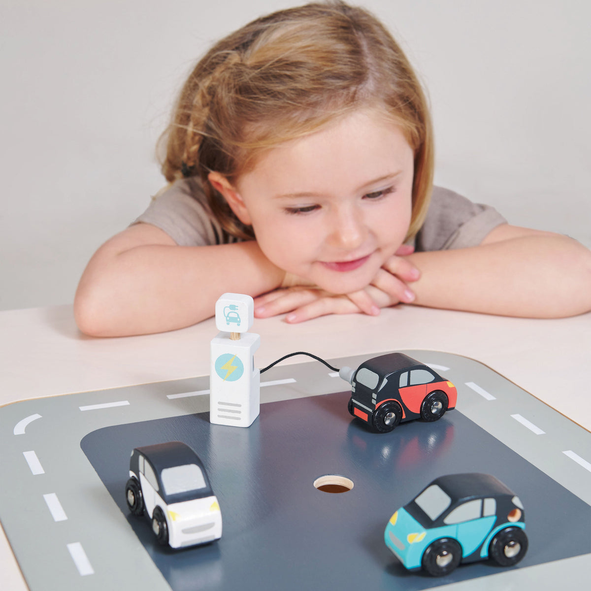 Child looking at three Smart Car Set toy cars and pretend charger on a road play surface