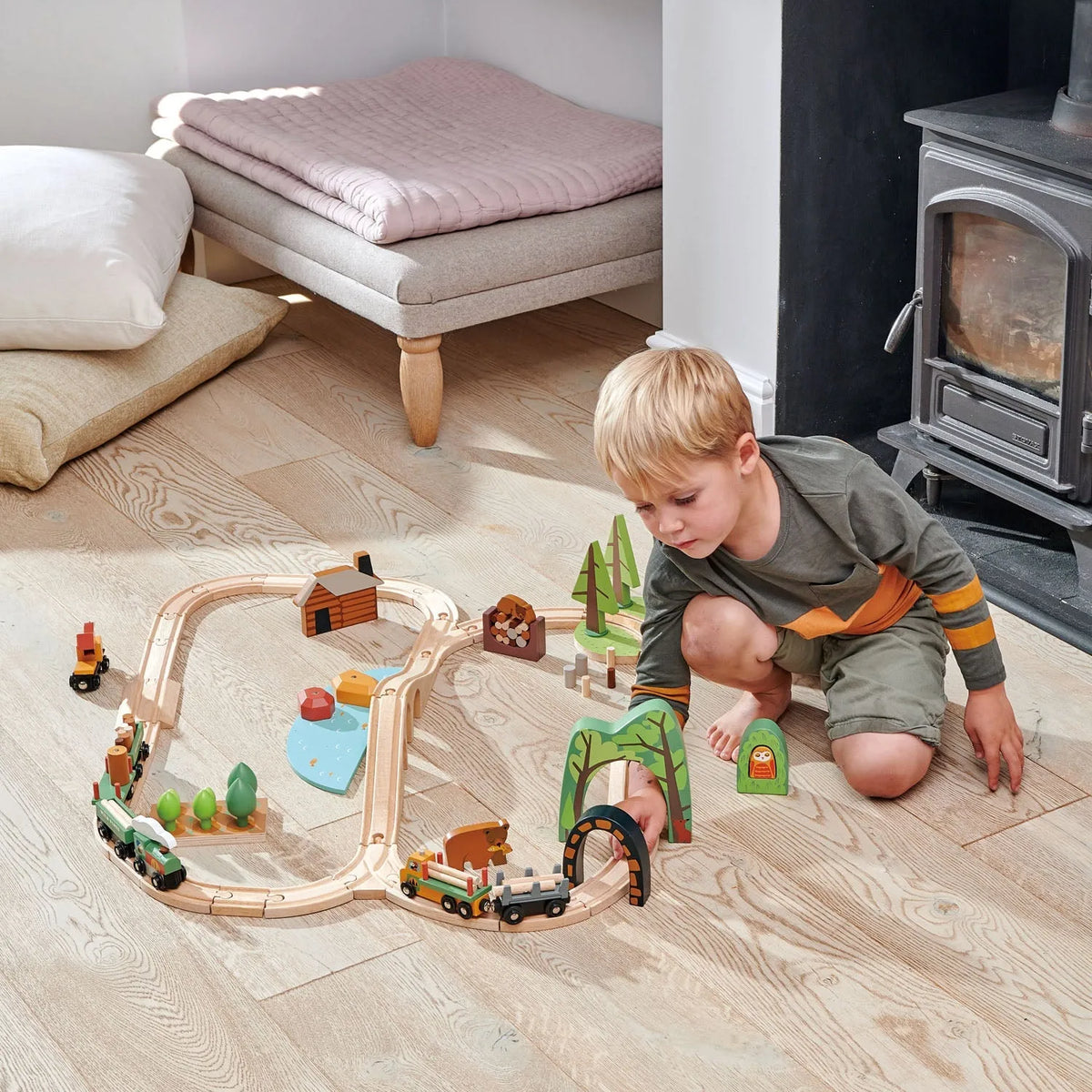 Child playing with a wooden toy train set on a wooden floor.