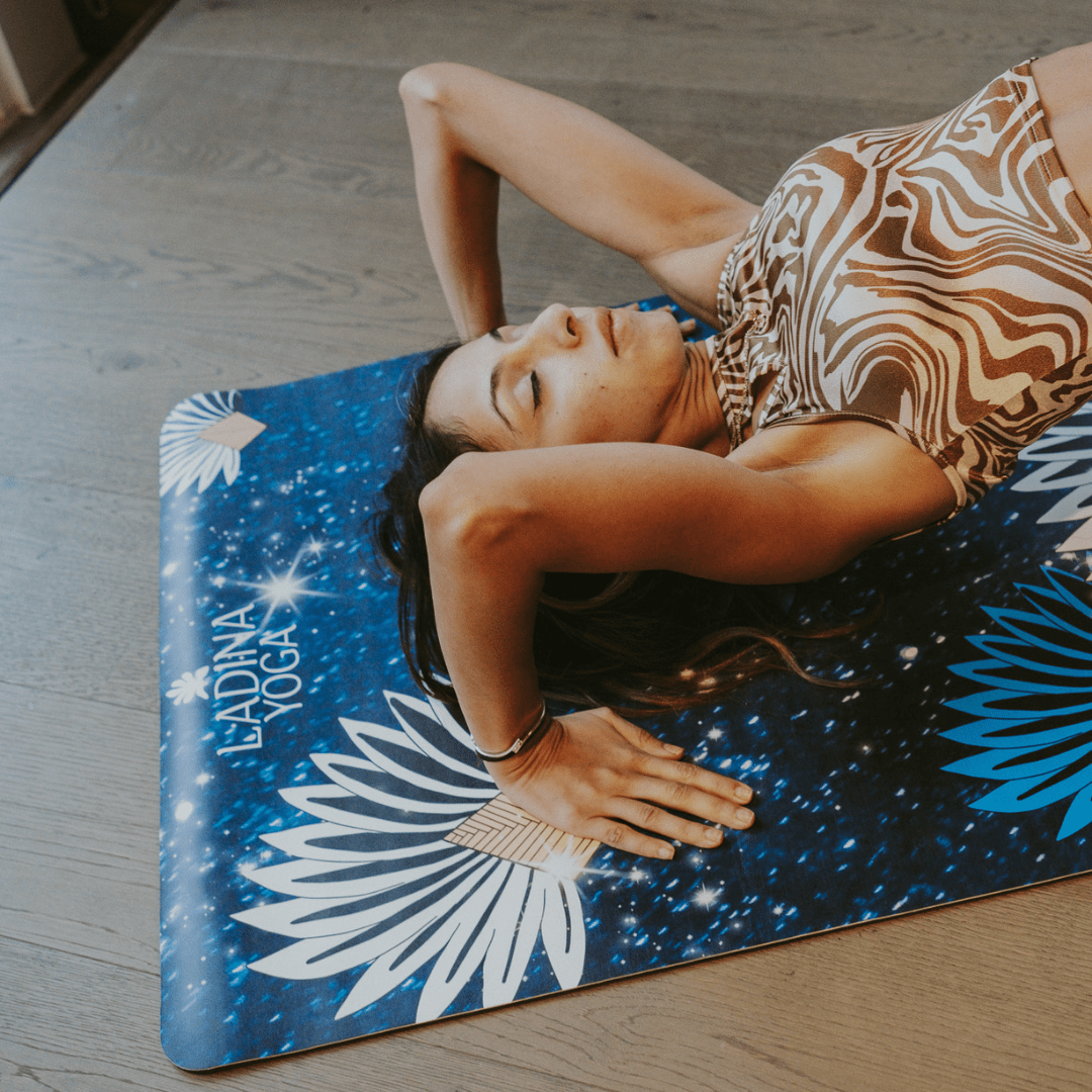 Woman lying on a blue and white floral-patterned yoga mat with 'Ladina Yoga' branding.