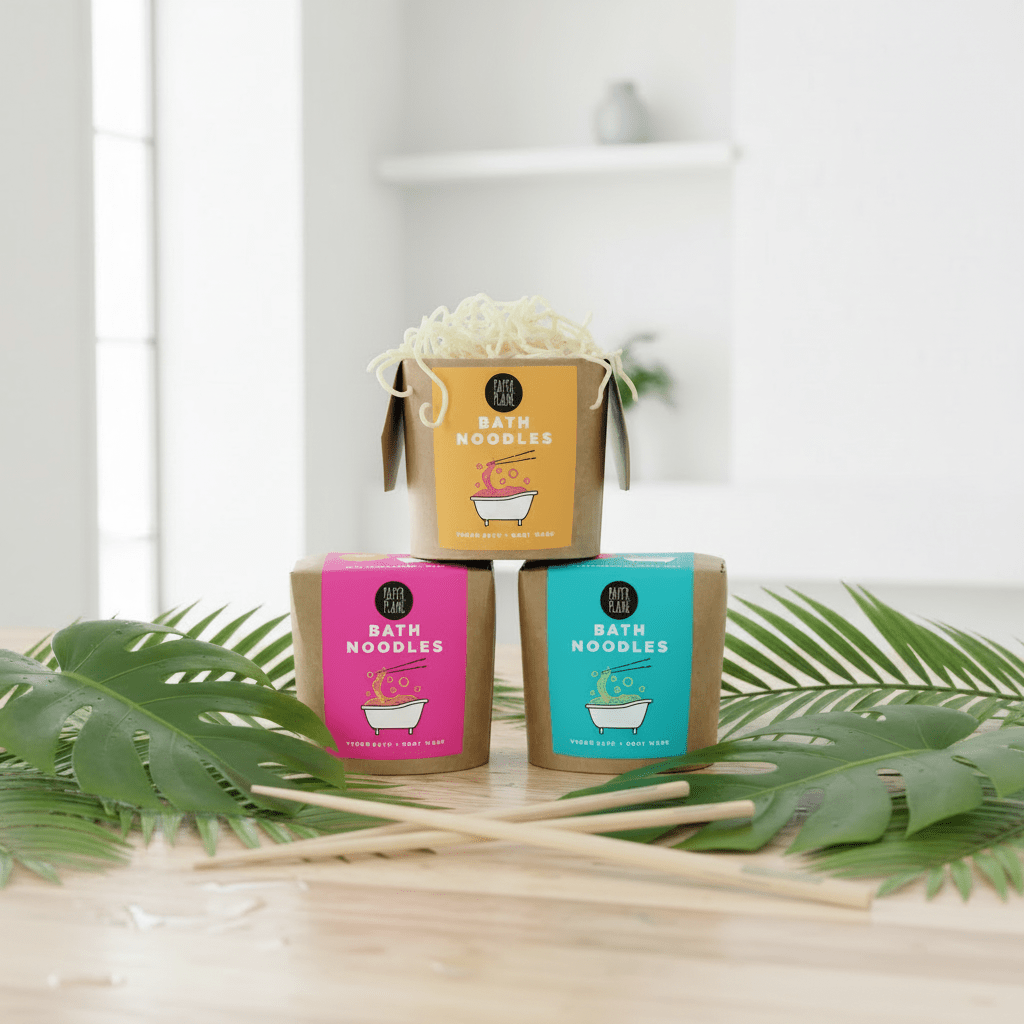 Three boxes of bath noodles with colorful labels on a wooden surface with green leaves.