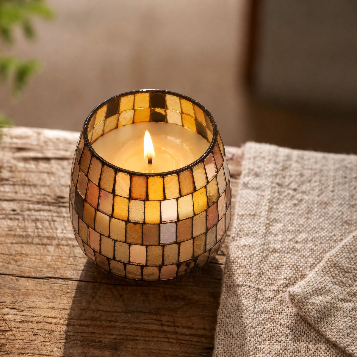 Mosaic candle holder with a lit candle on a wooden surface