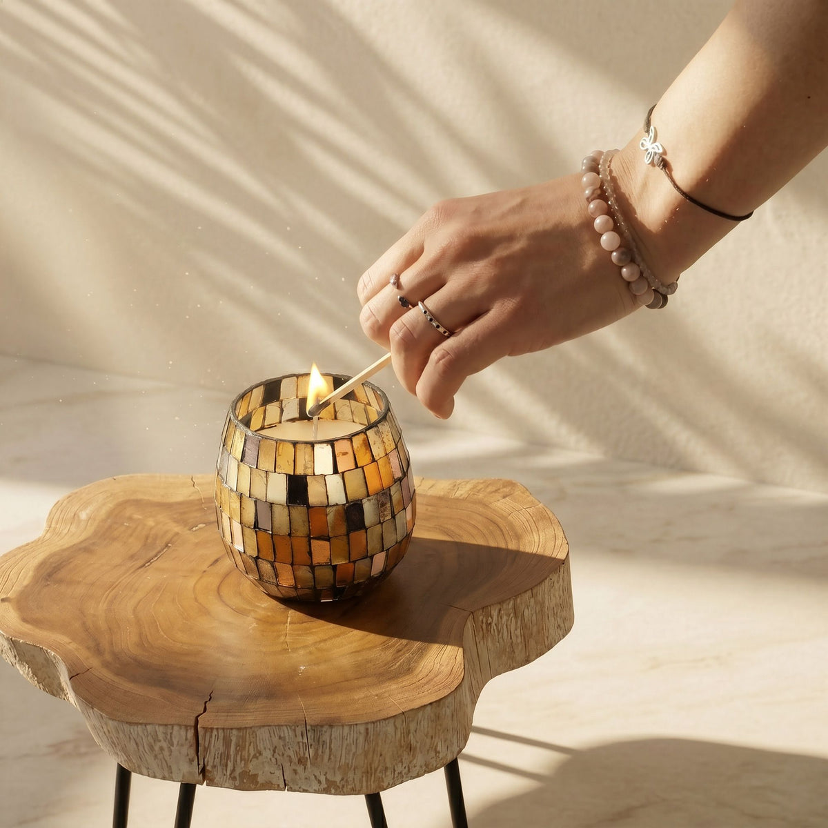 Hand lighting a candle in a mosaic glass holder on a wooden surface with a soft background