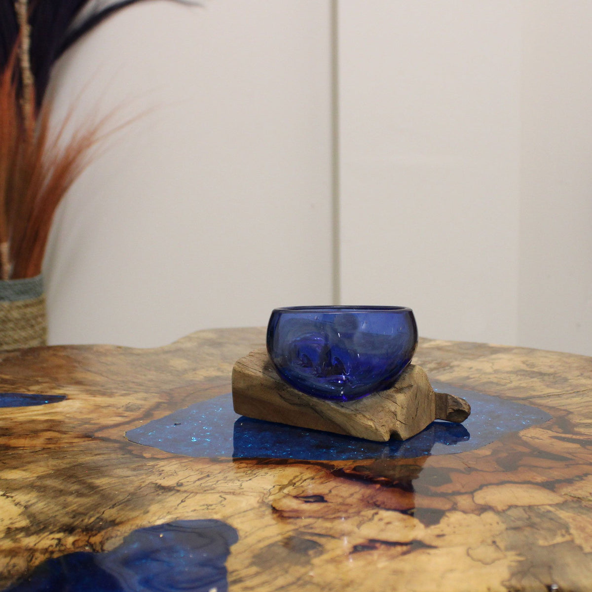 Mini blue glass bowl on a wooden base displayed on a wood and blue resin table