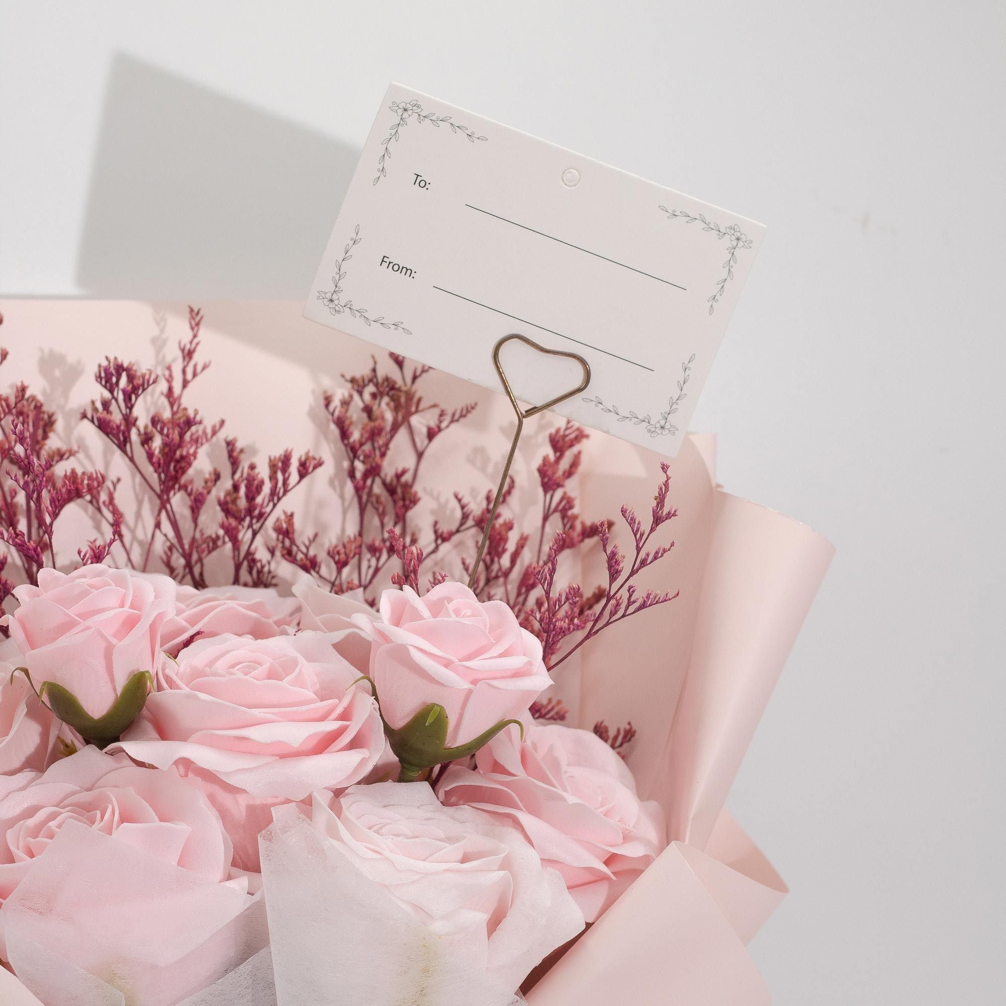 Bouquet of pink roses with a card and heart-shaped clip on a light background