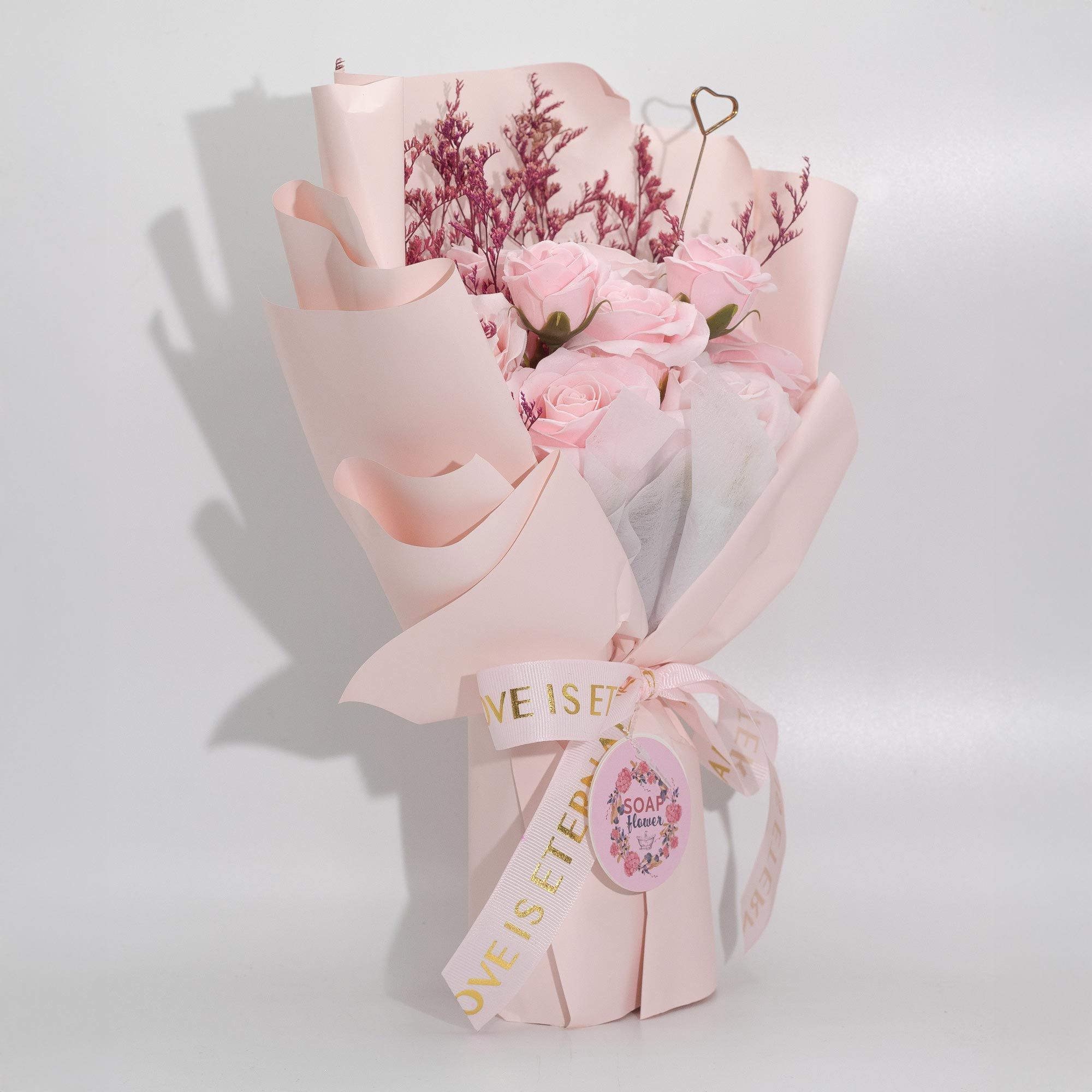 Bouquet of pink rose soap roses wrapped in pink paper with a ribbon on a white background