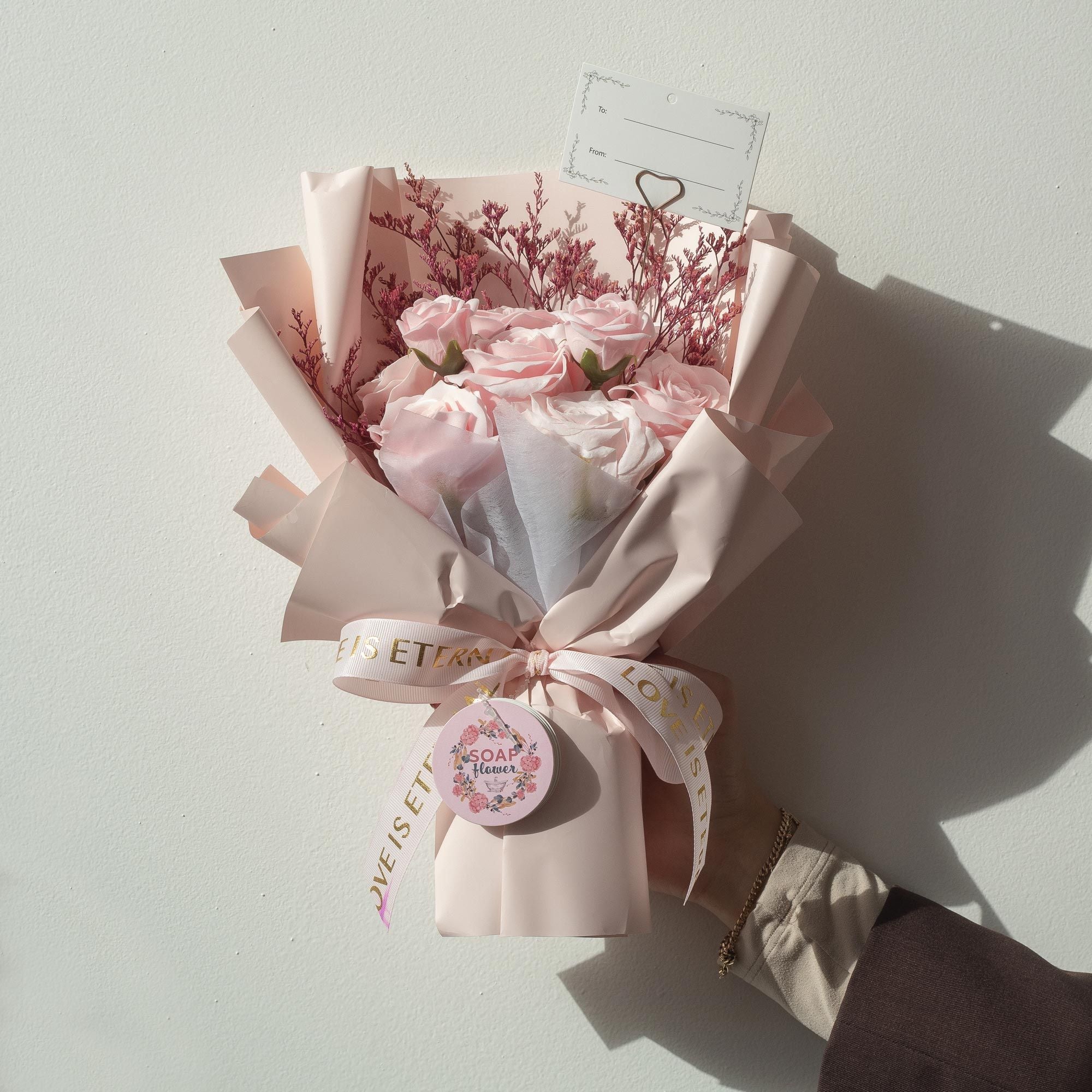 Bouquet of pink flowers wrapped in paper with a ribbon on a light gray background
