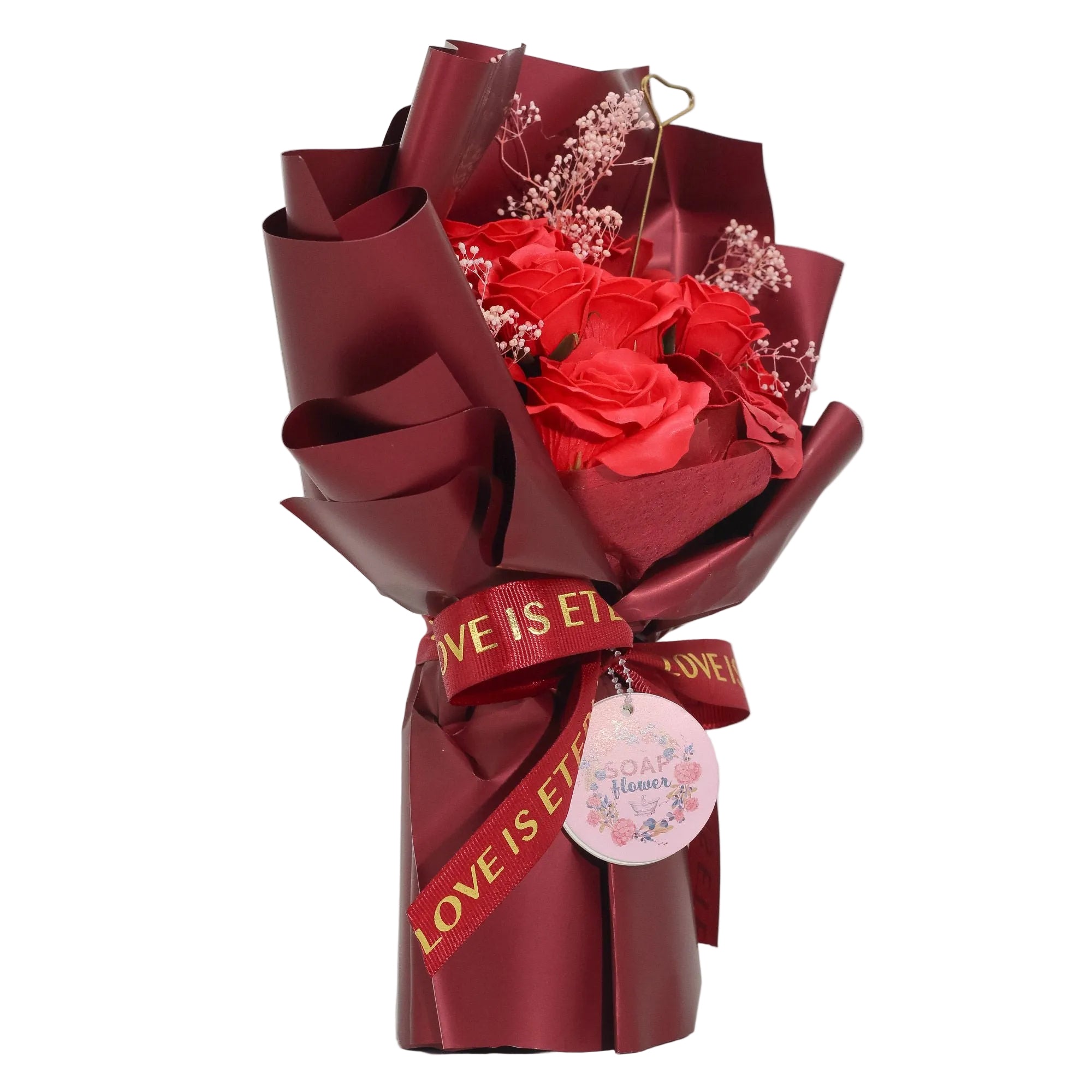 Bouquet of red soap roses wrapped in red paper with 'LOVE IS ETERNAL' ribbon on a white background