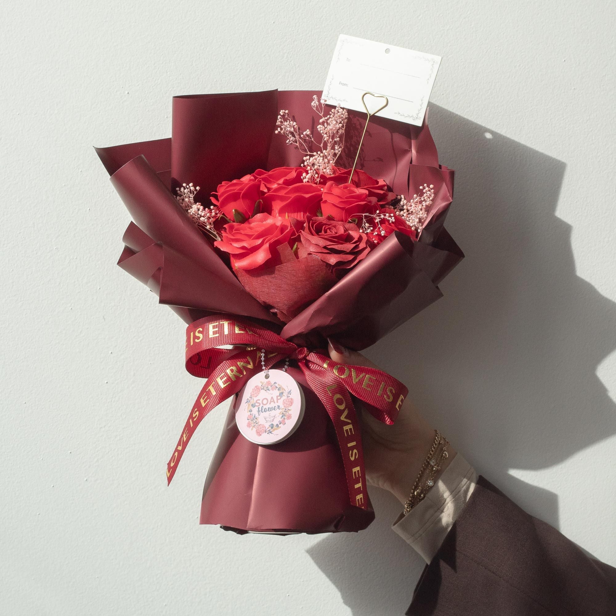 Bouquet of red soap roses wrapped in maroon paper with a decorative ribbon on a white background