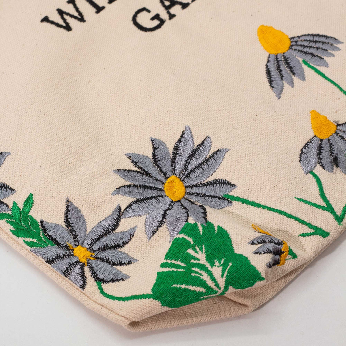Close-up of purple-grey flower embroidery with yellow centres and green leaves on the natural cotton tote