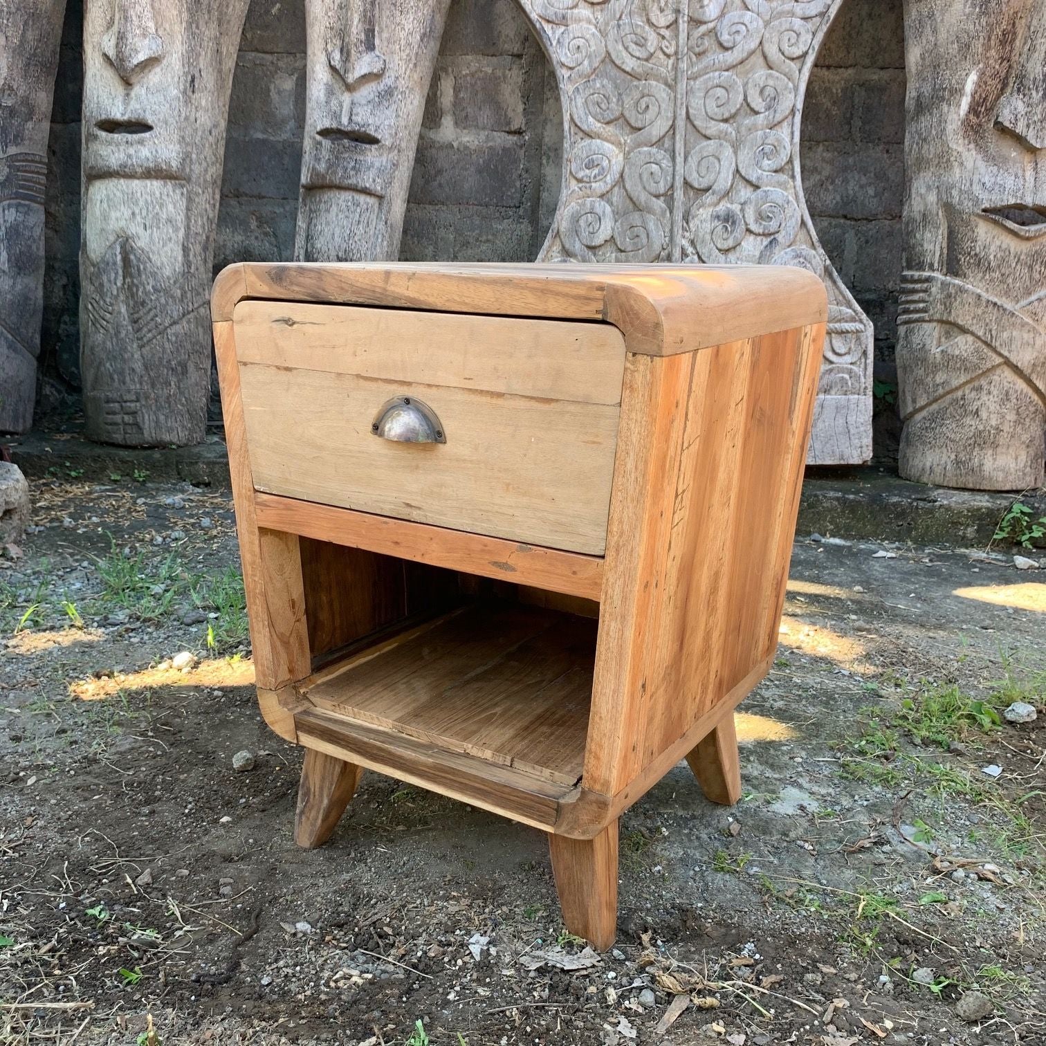Wooden nightstand with a single drawer in front of stone carvings