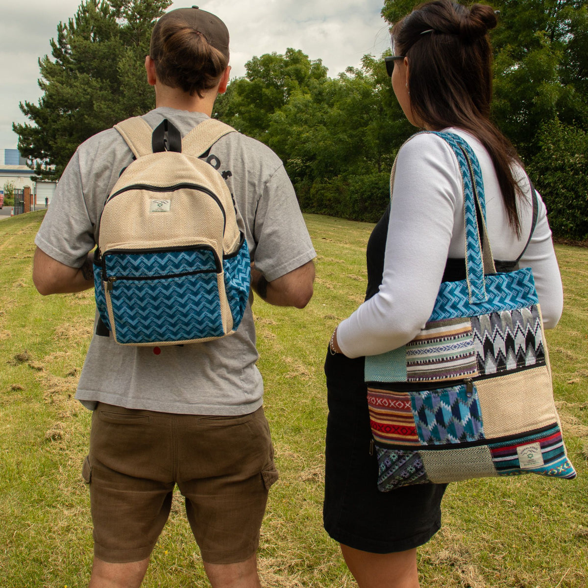 Two people outdoors, one wearing a blue-patterned backpack and the other carrying the Kathmandu patchwork tote