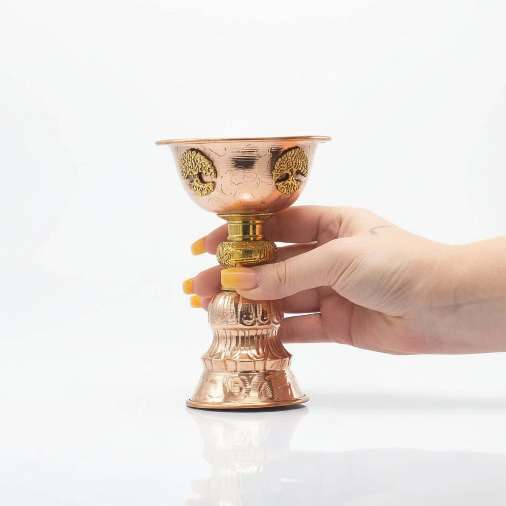 Hand holding a copper and gold decorative ritual goblet against a white background