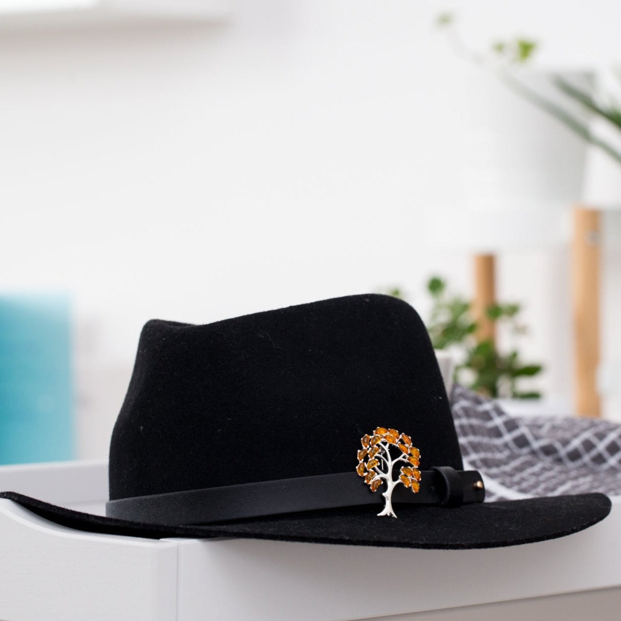 Black hat with a decorative brooch on a white surface with a blurred background