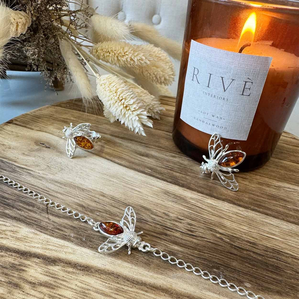 Silver bee jewellery with amber stones on a wooden surface next to a lit candle.