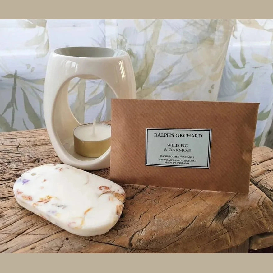 Candle, candle holder, and box labeled 'Ralph's Orchard' on a wooden surface with a natural background.
