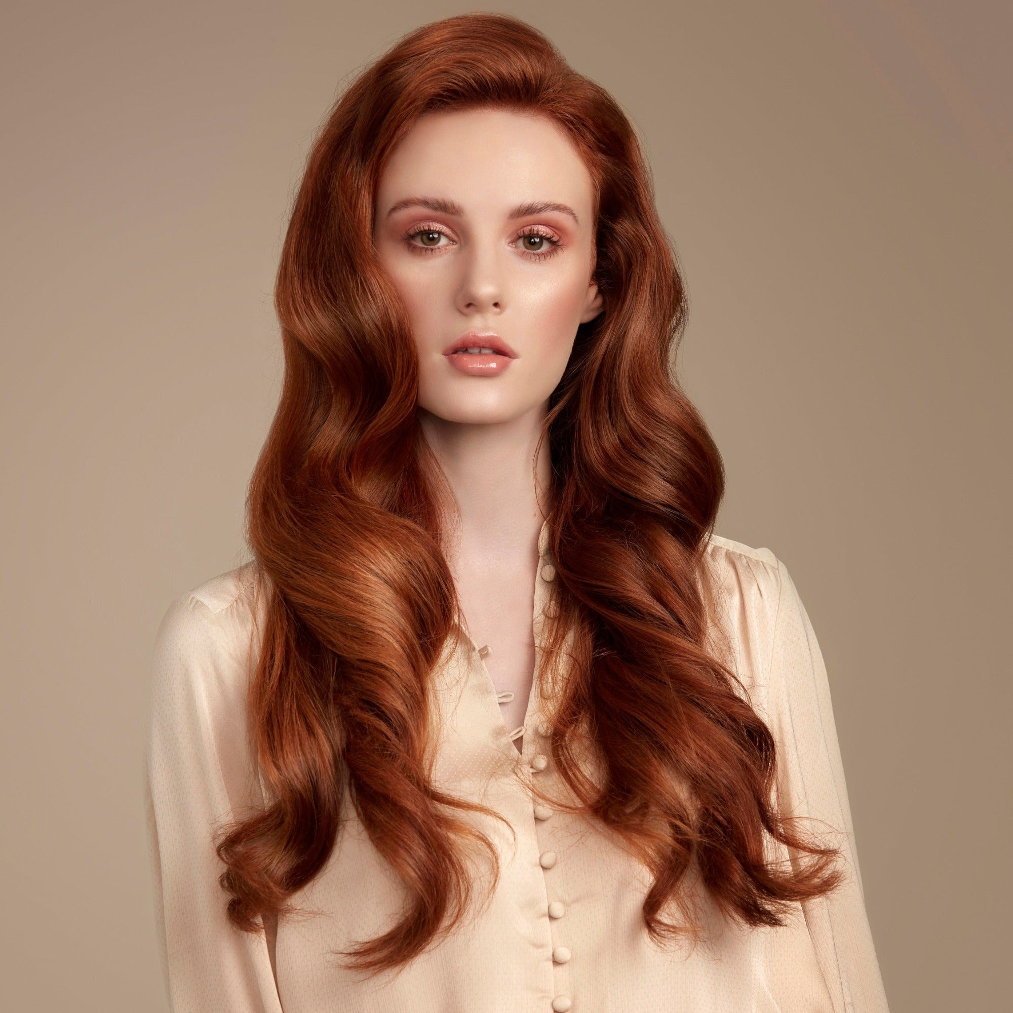Woman with long wavy red hair wearing a beige blouse against a neutral background