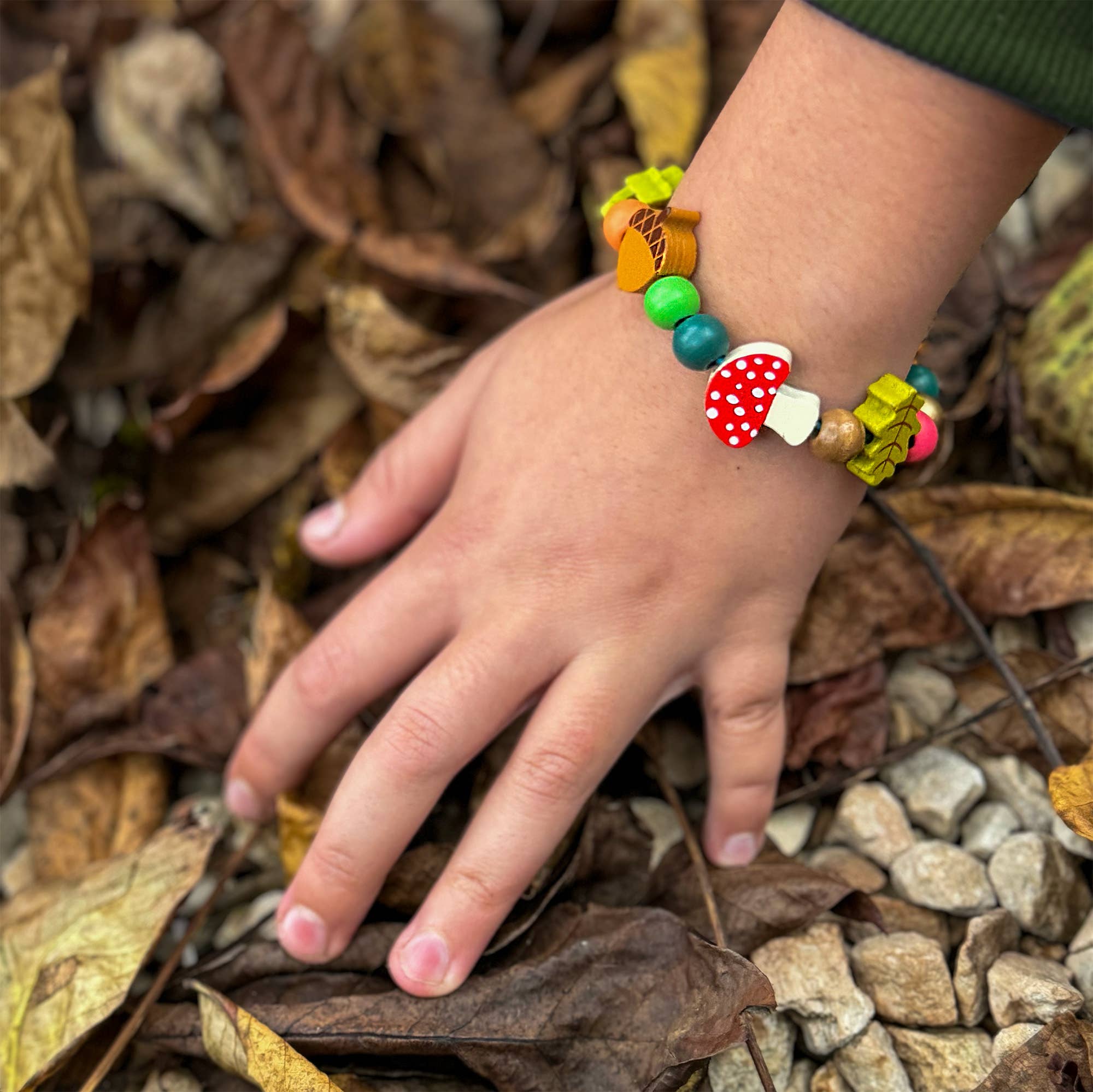 Forest-themed bracelet on a child's wrist with bark and leaves in the background.