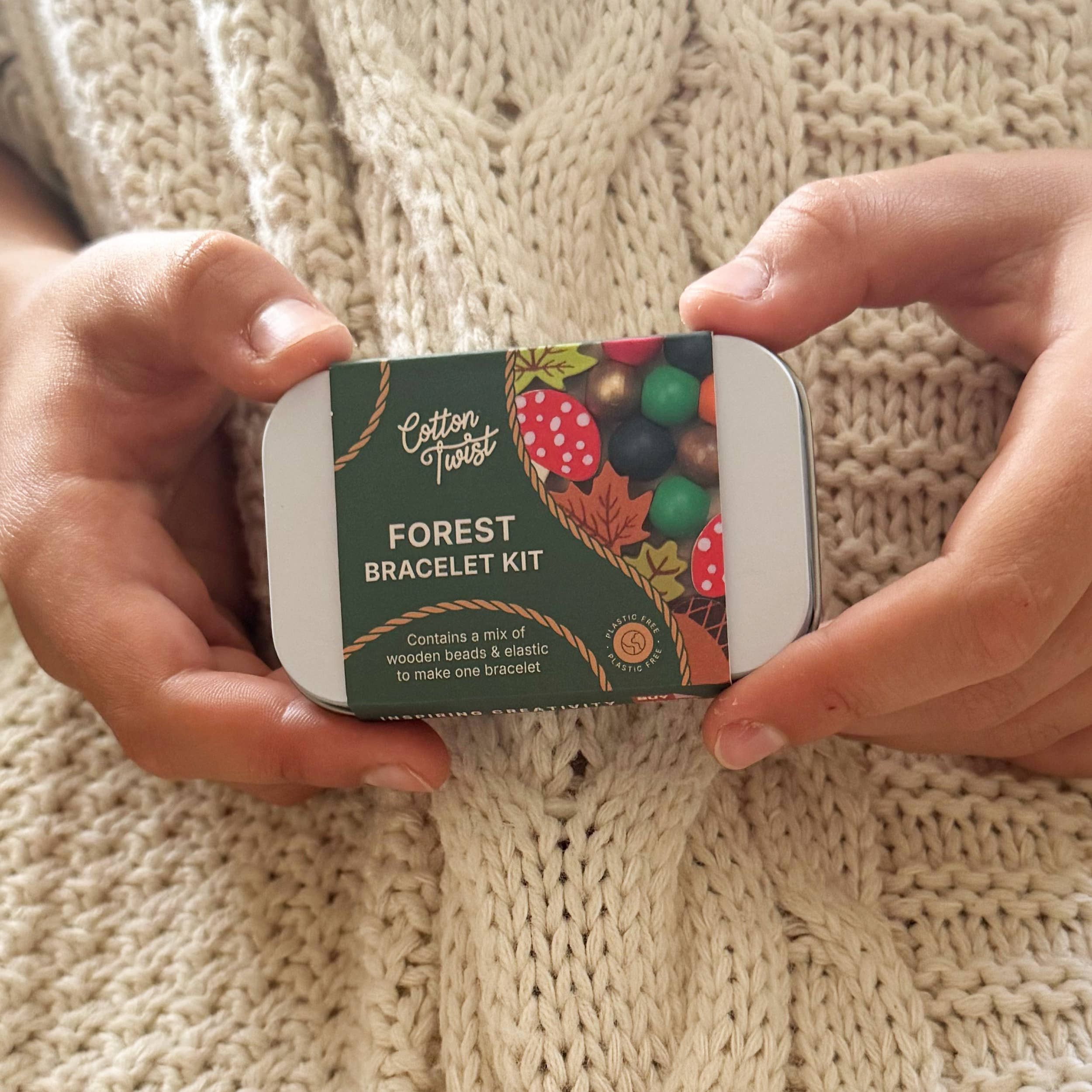 Forest-themed bracelet kit in a tin, held by a person in a cream aran jumper.