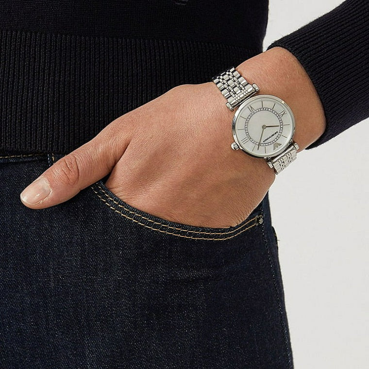 Hand wearing a silver watch with a white face, against a neutral background