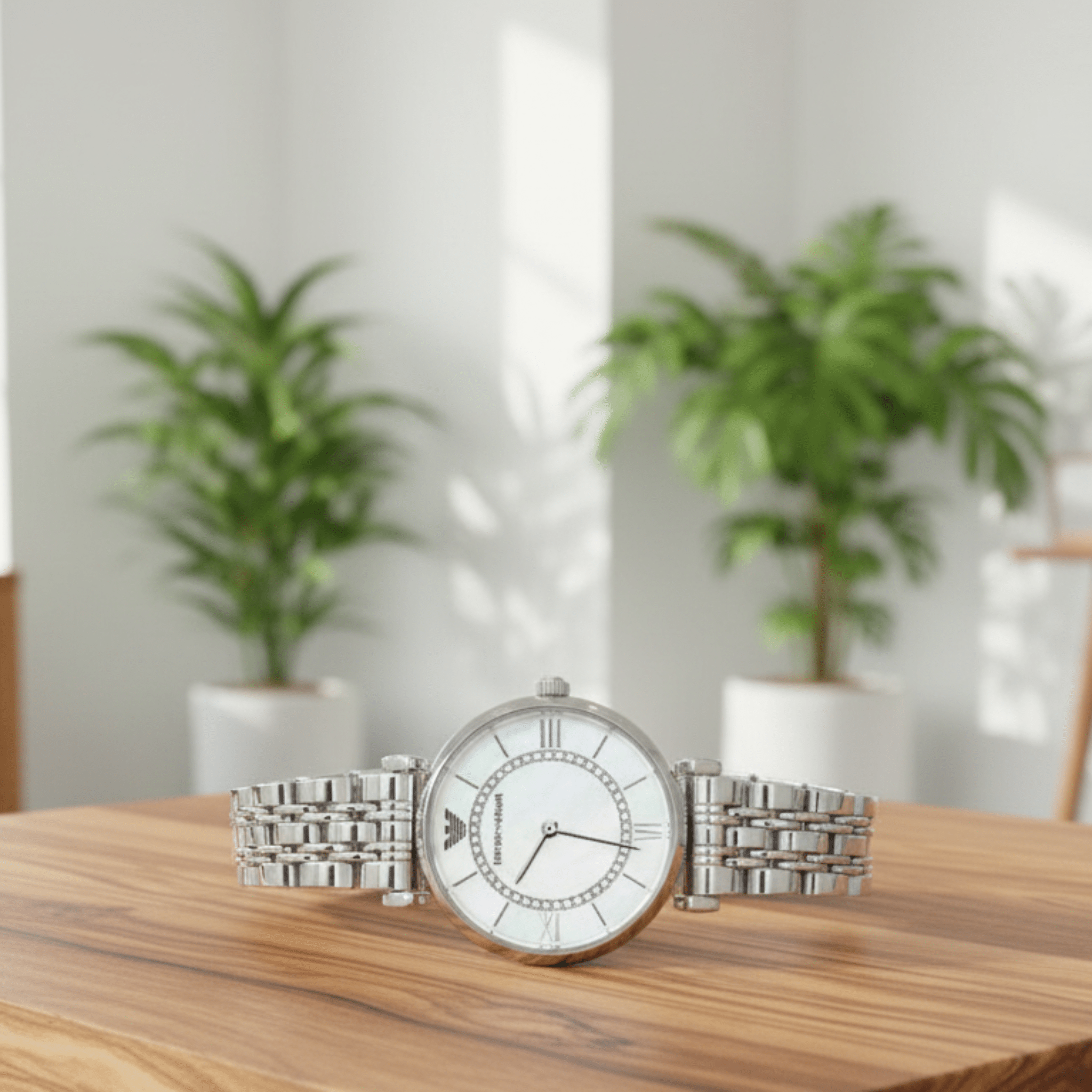 Silver watch with a white face on a wooden surface with blurred plants in the background