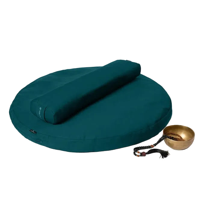 Teal meditation cushion with rolled-up mat and brass singing bowl on a light gray background