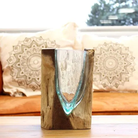 Glass and wood art vase displayed on a table in front of patterned cushions.